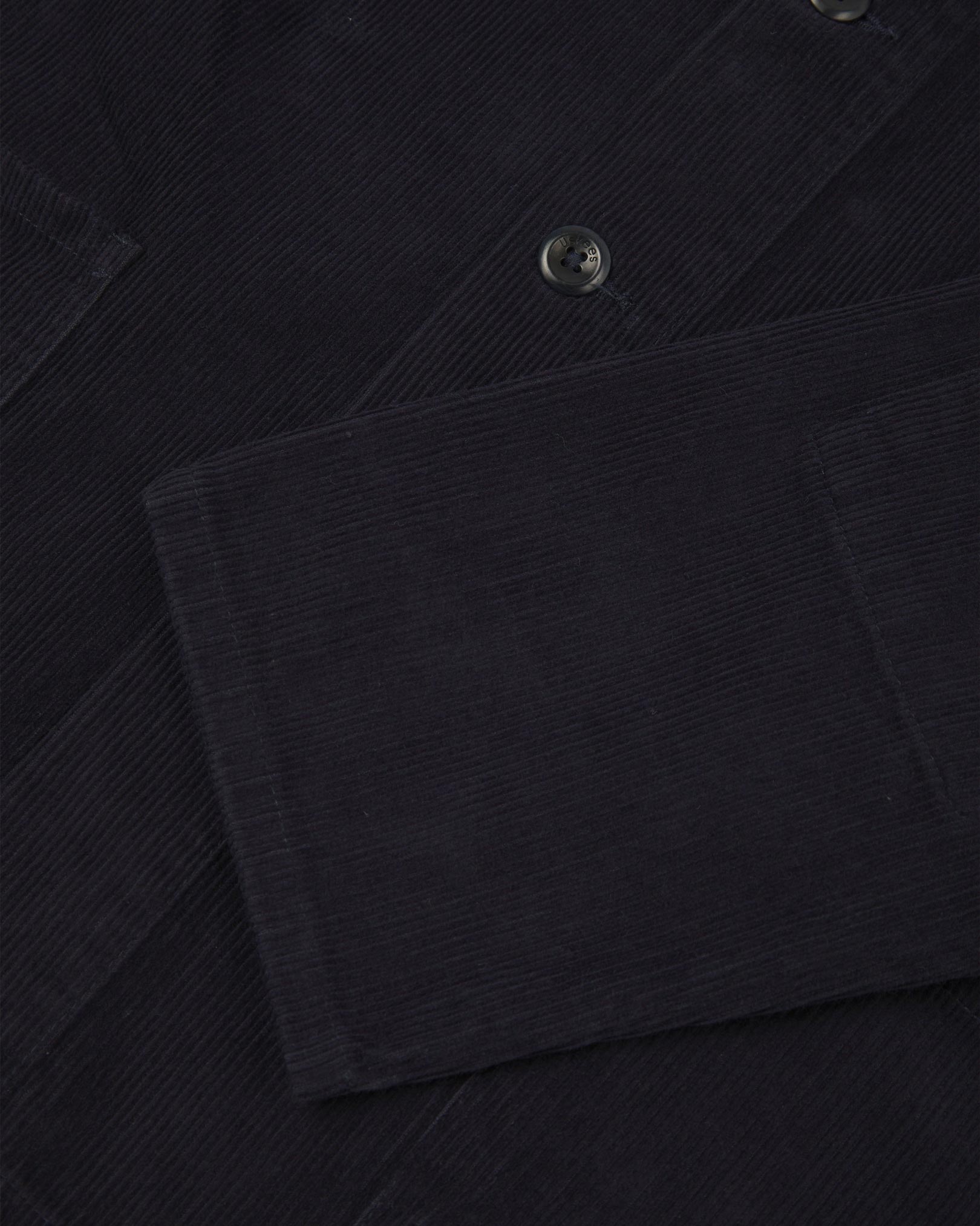 Closer view of mid section of midnight blue, buttoned corduroy overshirt from Uskees. Focus on cuff, pockets, corozo buttons and corduroy texture.