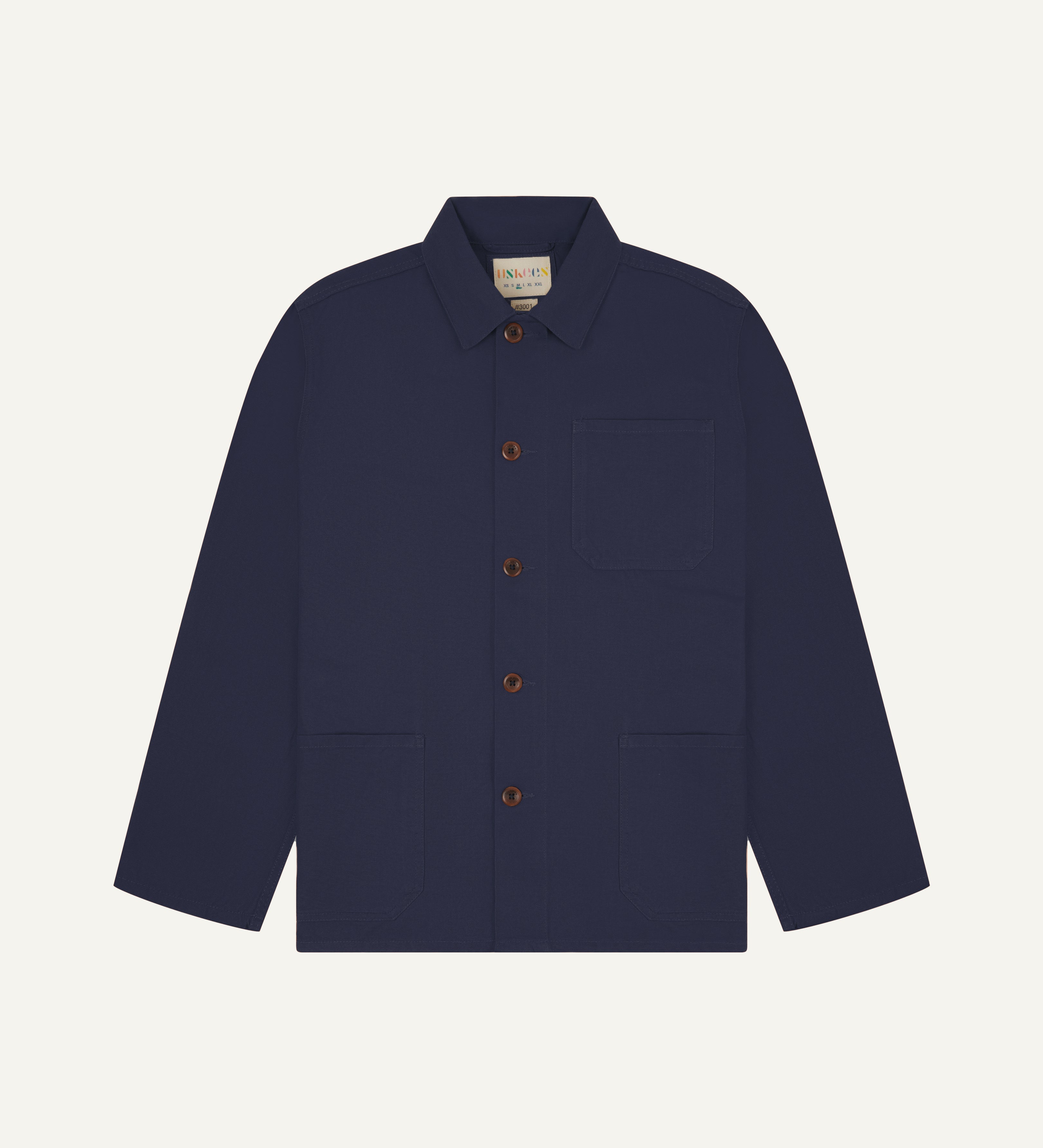 Front flat shot of midnight blue, buttoned organic cotton overshirt. Clear view of chest and hip pockets, corozo buttons and Uskees branding label.