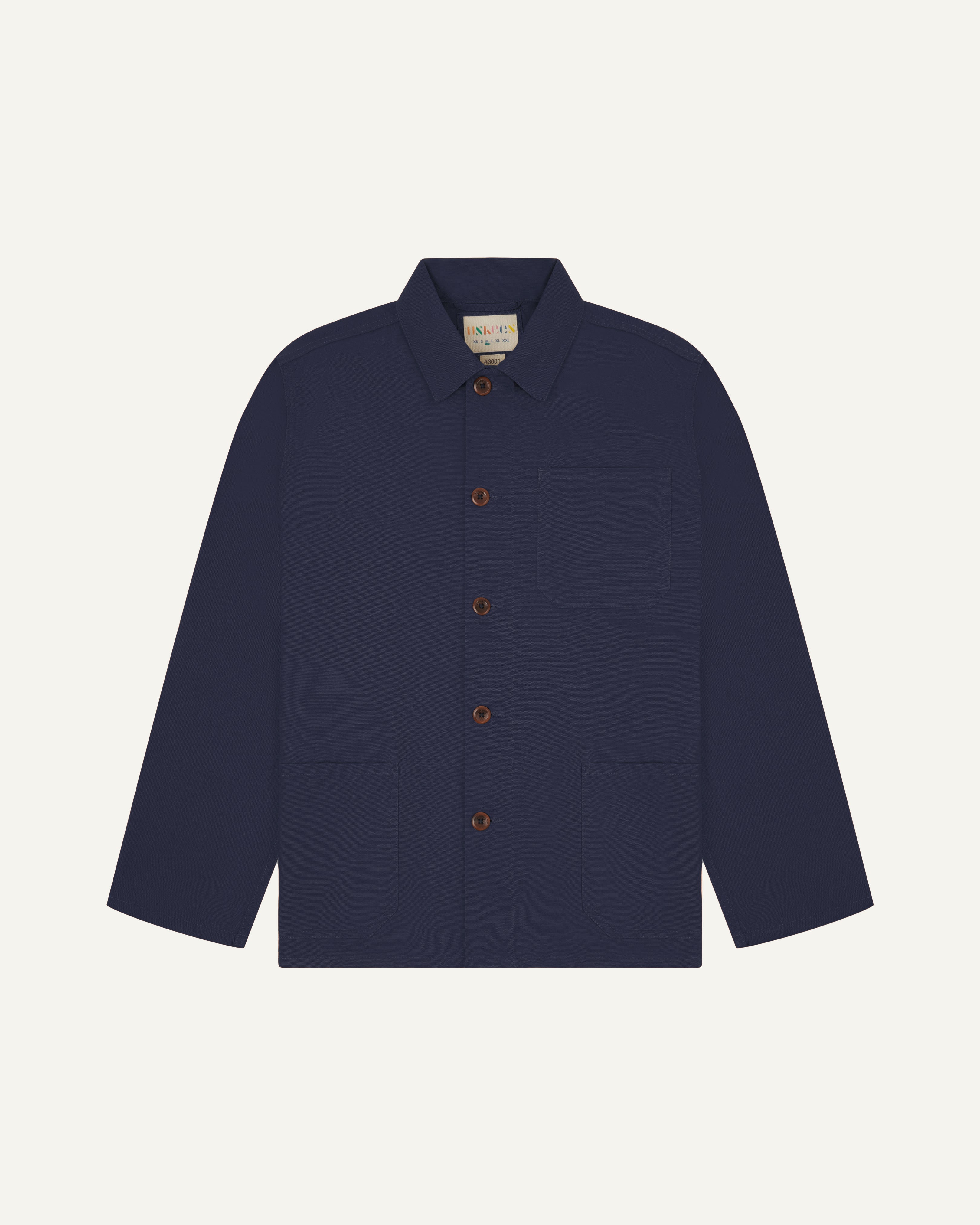 Front flat shot of midnight blue, buttoned organic cotton overshirt. Clear view of chest and hip pockets, corozo buttons and Uskees branding label.