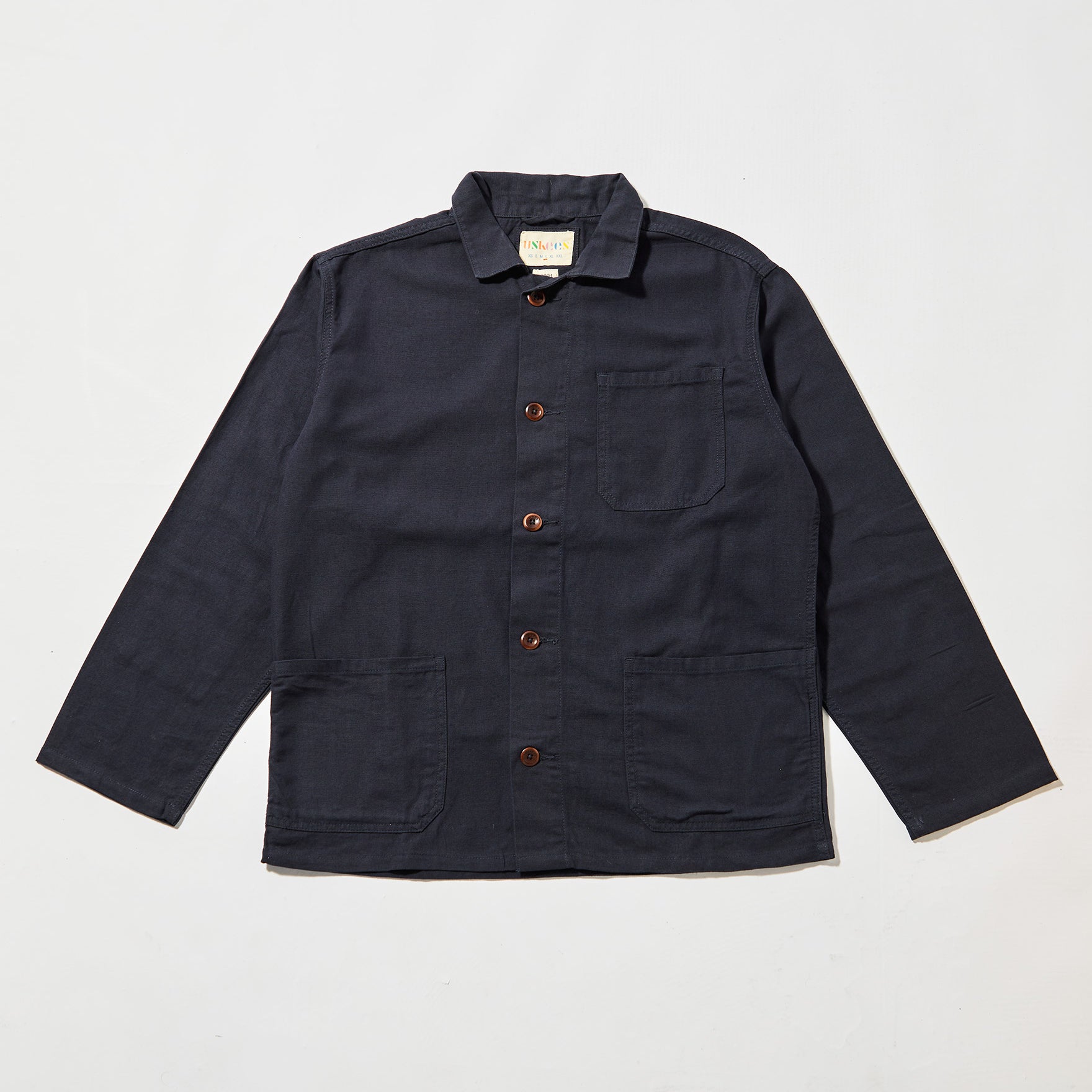 Front flat shot of midnight blue, buttoned organic cotton overshirt. Clear view of chest and hip pockets, corozo buttons and Uskees branding label.  Zero waste production.