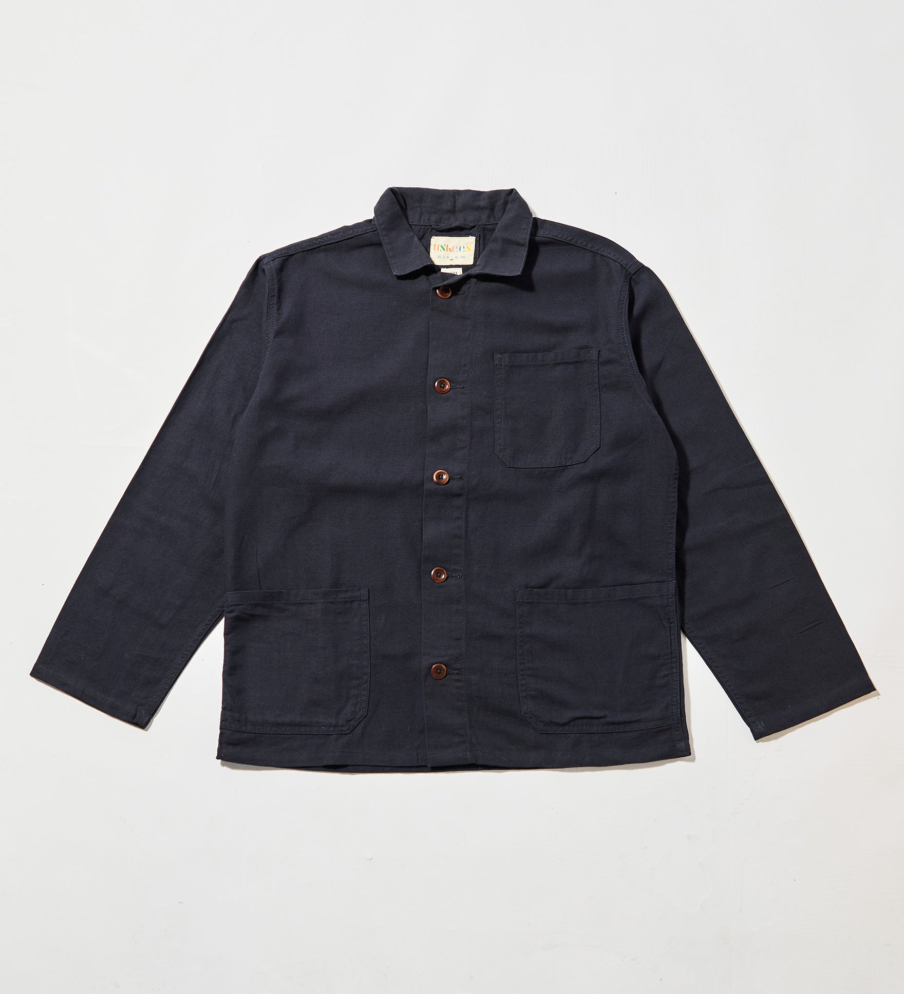 Front flat shot of midnight blue, buttoned organic cotton overshirt. Clear view of chest and hip pockets, corozo buttons and Uskees branding label.  Zero waste production.