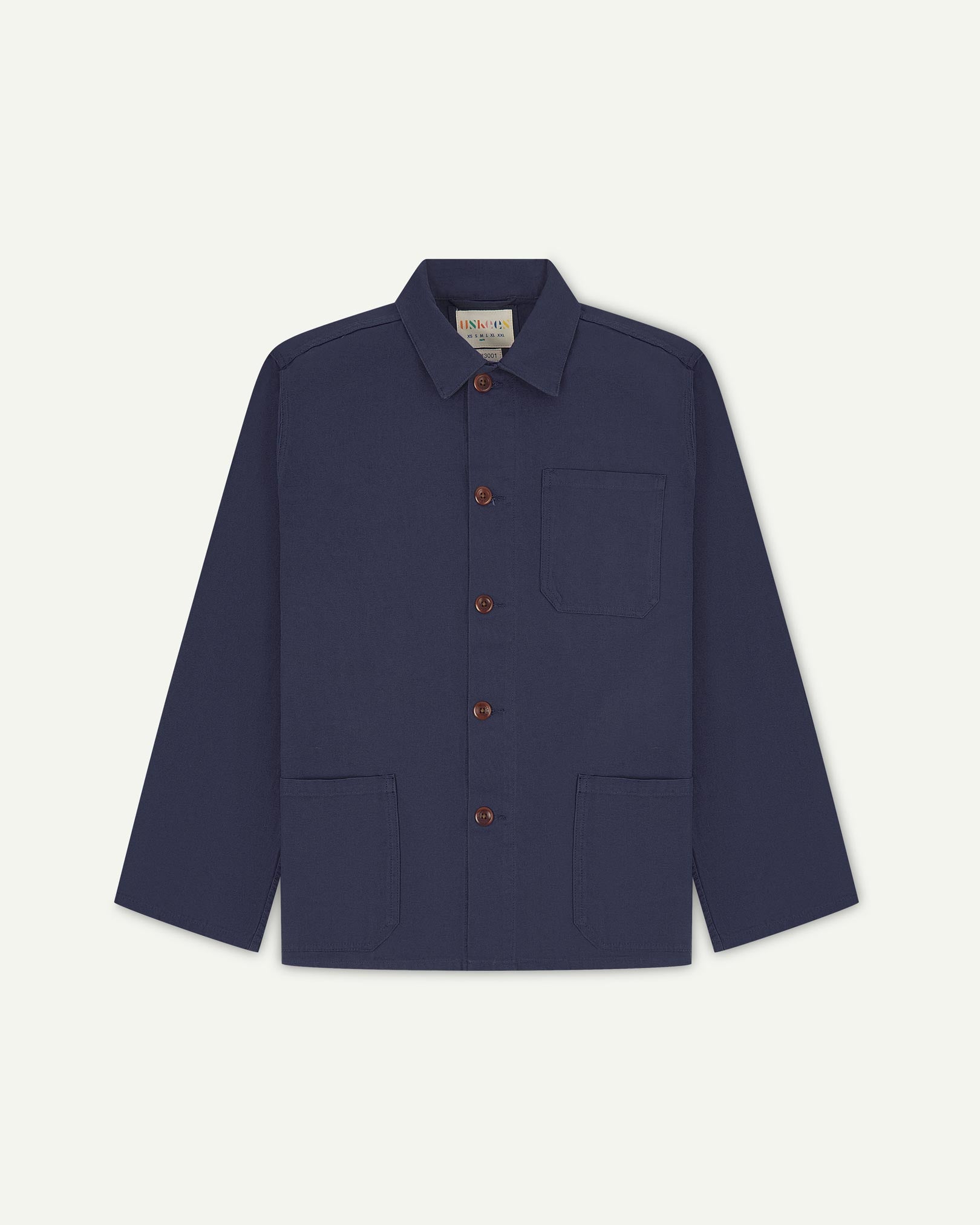 Front flat shot of midnight blue, buttoned organic cotton overshirt. Clear view of chest and hip pockets, corozo buttons and Uskees branding label.