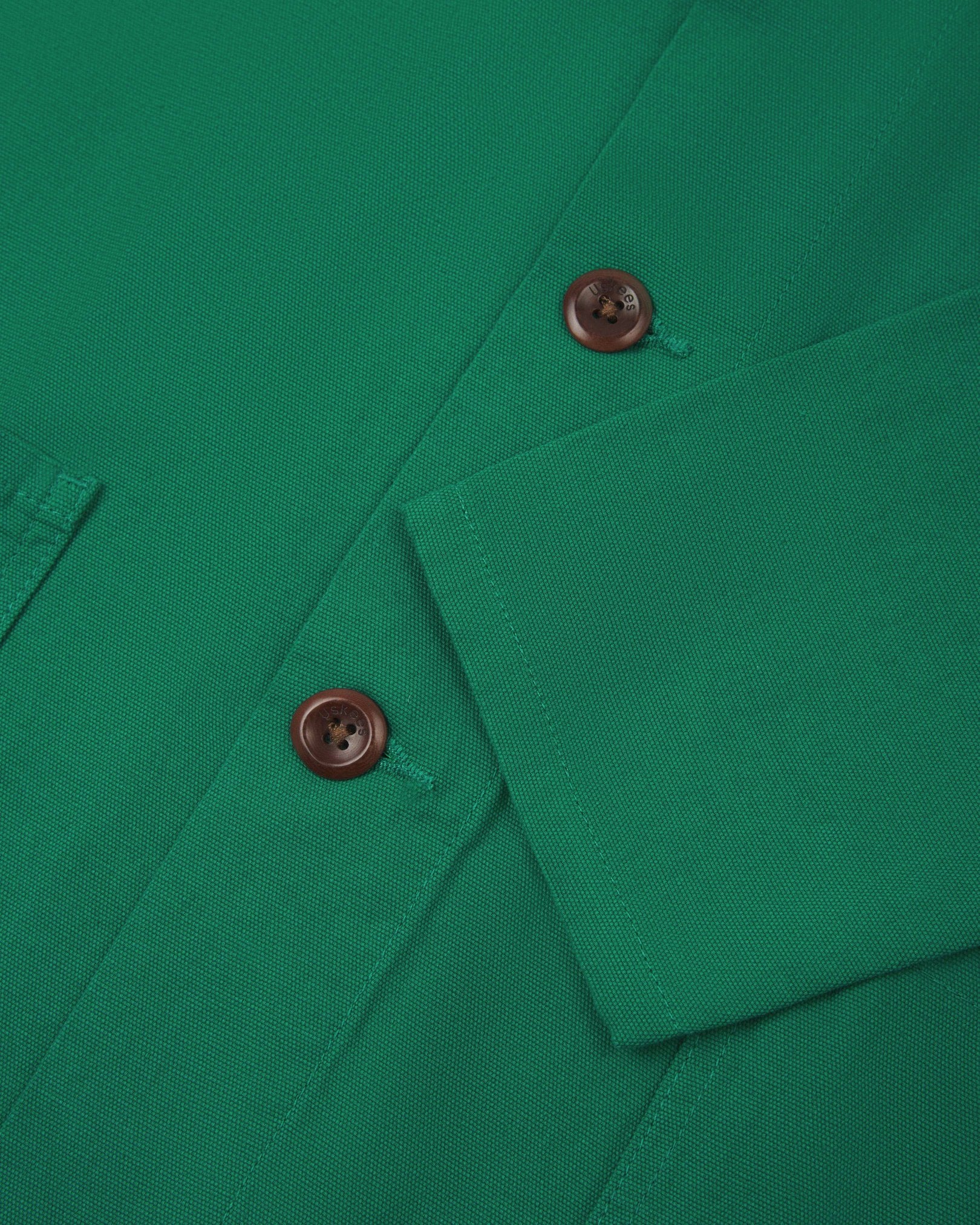 Closer view of mid section of mint green, buttoned organic cotton overshirt from Uskees. Focus on cuff, placket and corozo buttons.