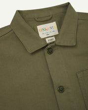 Close-up top-half view of #3001, moss-green organic cotton drill overshirt. With focus on collar, Uskees brand label and corozo buttons.