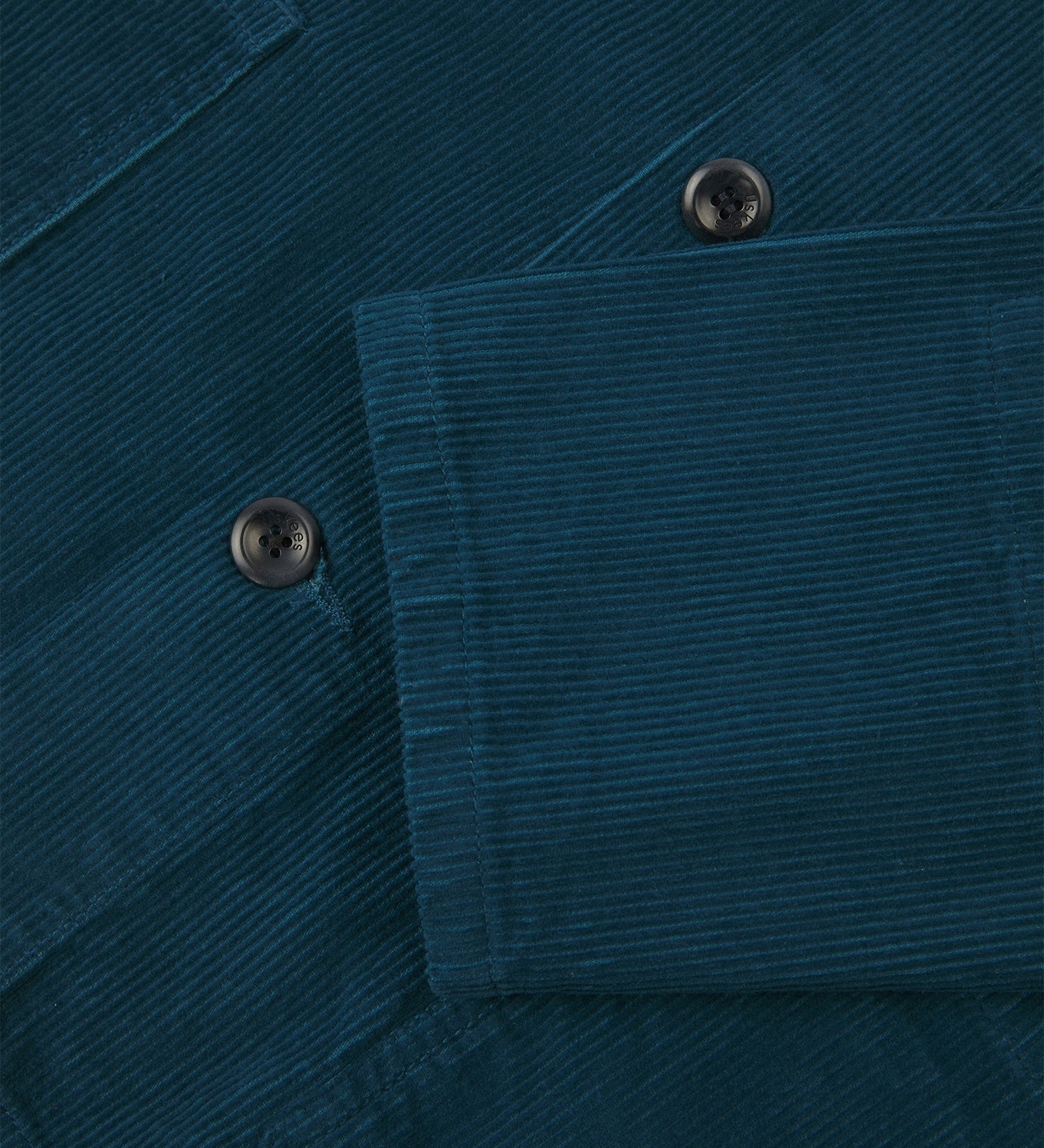 Closer view of mid section of petrol blue, buttoned corduroy overshirt from Uskees. Focus on cuff, pockets, corozo buttons and corduroy texture.