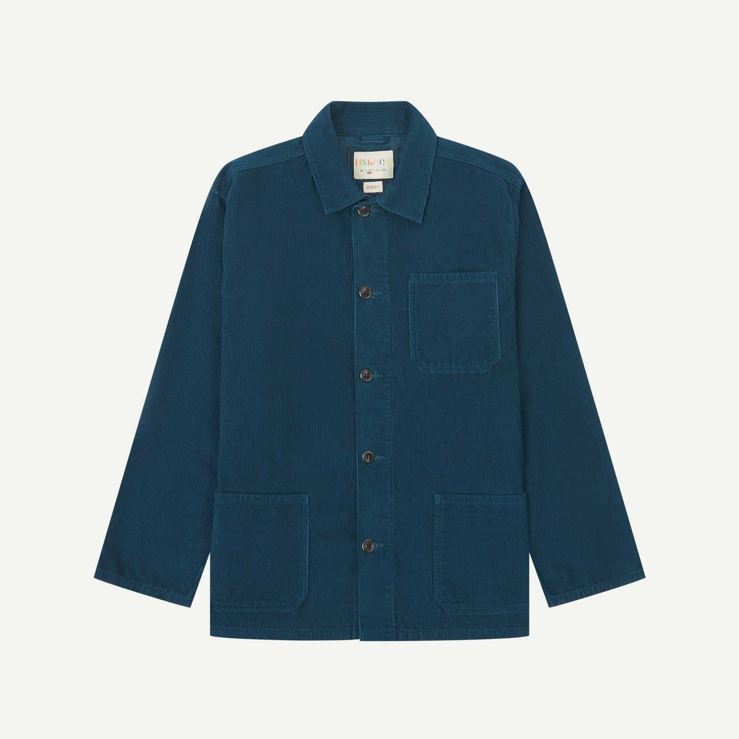 Front flat shot of petrol blue, buttoned corduroy overshirt. Clear view of chest and hip pockets, corozo buttons and Uskees branding label.