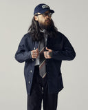 Front model shot of Uskees raw orta denim shirt-jacket paired with cap and tie.