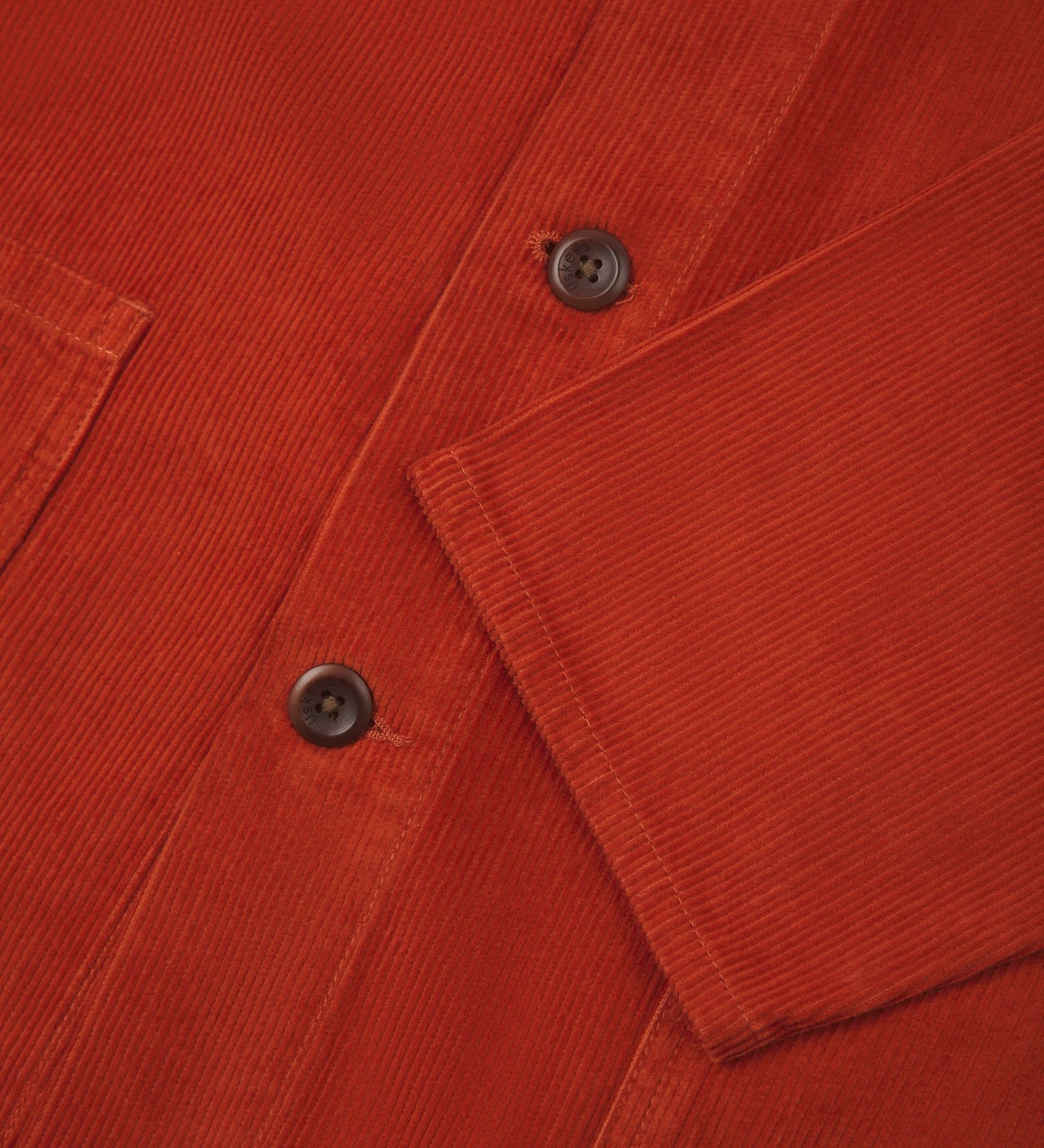 Closer view of mid section of rust-red, buttoned corduroy overshirt from Uskees. Focus on cuff, pockets, corozo buttons and corduroy texture.