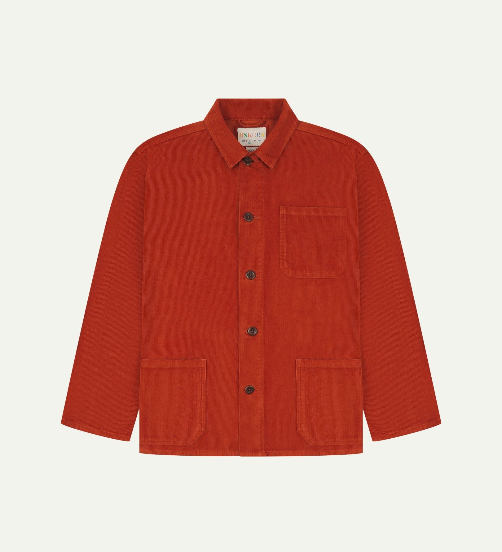 Front flat shot of rust-red, buttoned corduroy overshirt. Clear view of chest and hip pockets, corozo buttons and Uskees branding label.