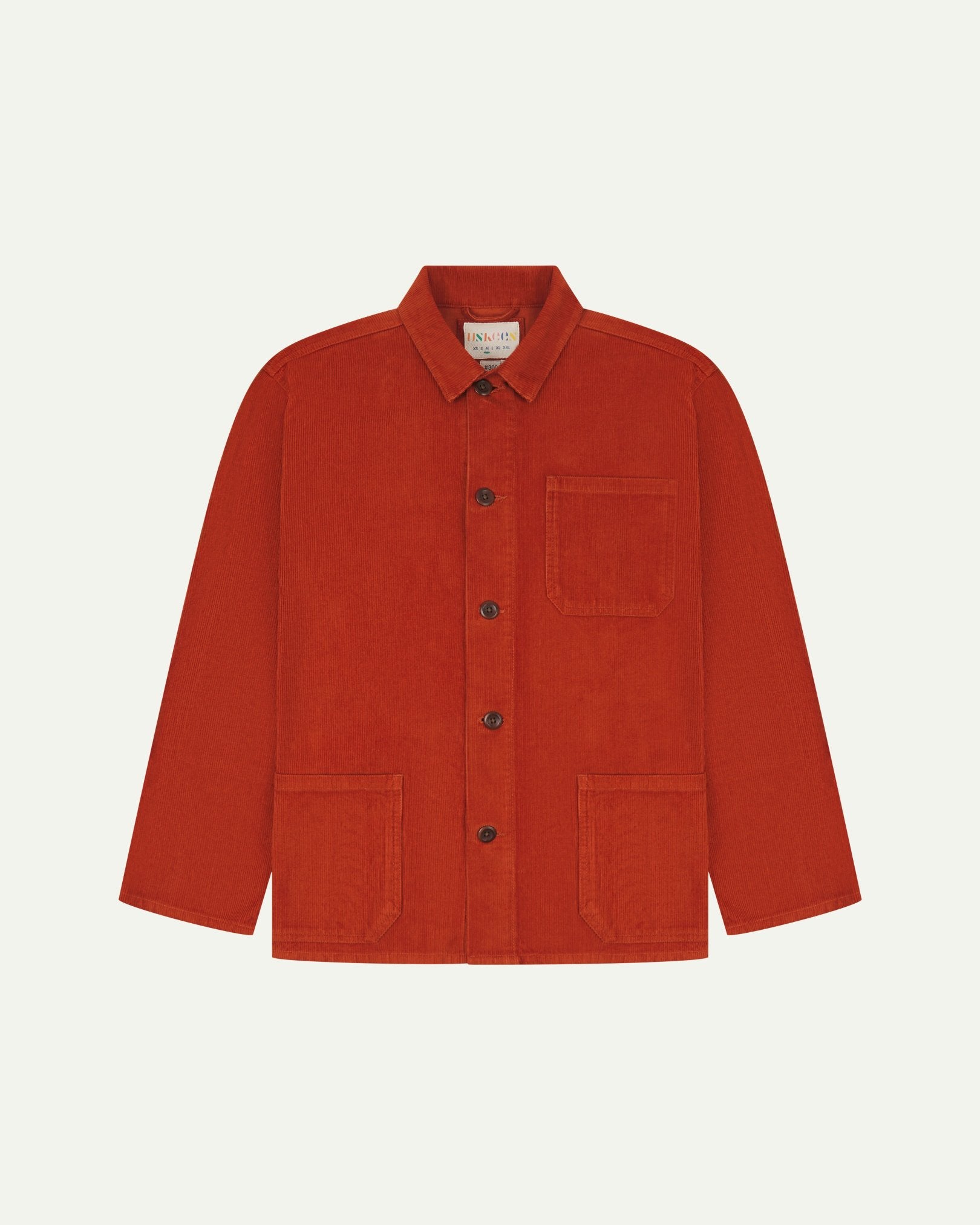 Front flat shot of rust-red, buttoned corduroy overshirt. Clear view of chest and hip pockets, corozo buttons and Uskees branding label.