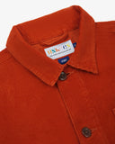 Close-up view of 3001 rust-red, buttoned corduroy overshirt from Uskees showing corozo buttons, brand/size label, collar and hanging loop.