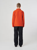 Full-length back view of man wearing an Uskees rust red-orange cotton overshirt paired with dark pants, showing reinforced elbows.
