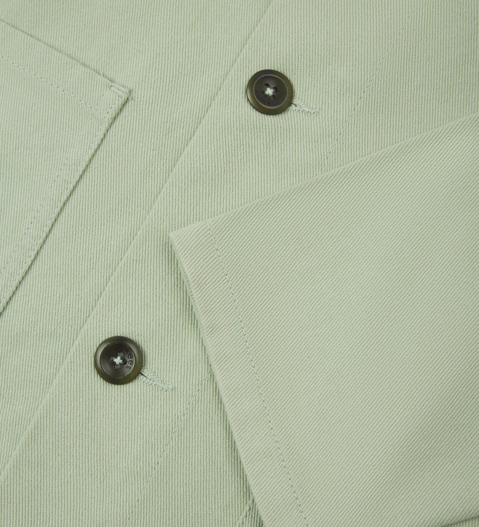 View of the mid-section and sleeve of the 3001 Uskees button-down drill overshirt in silver-green with focus on cuff, placket and hip pocket.