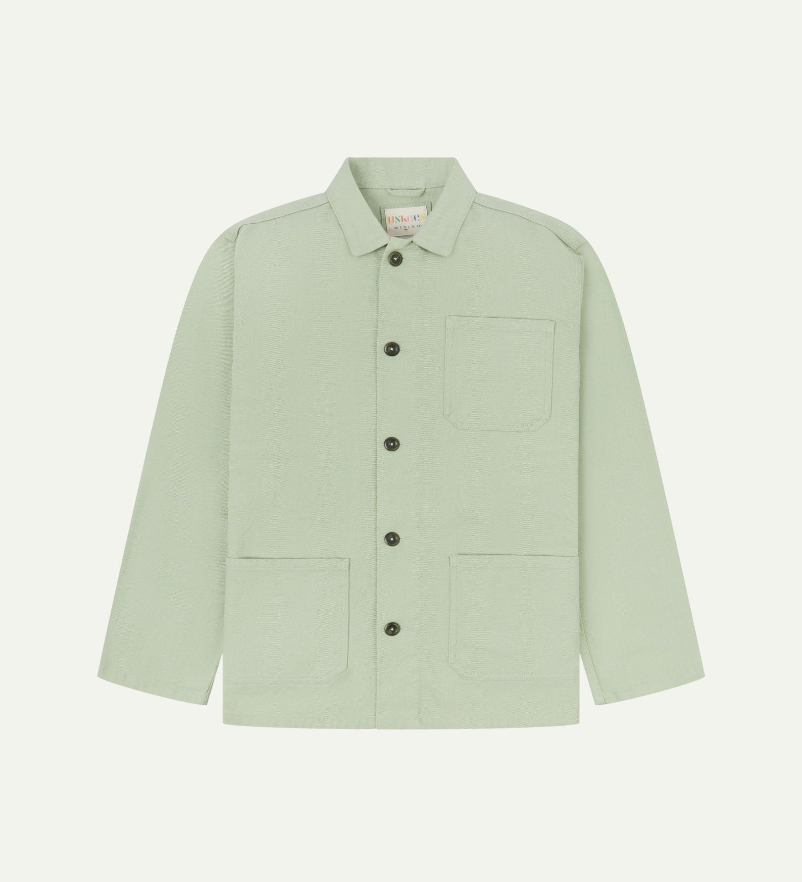 Front flat shot of silver-green, buttoned drill overshirt. Clear view of corozo buttons, 3 pockets and Uskees branding label.