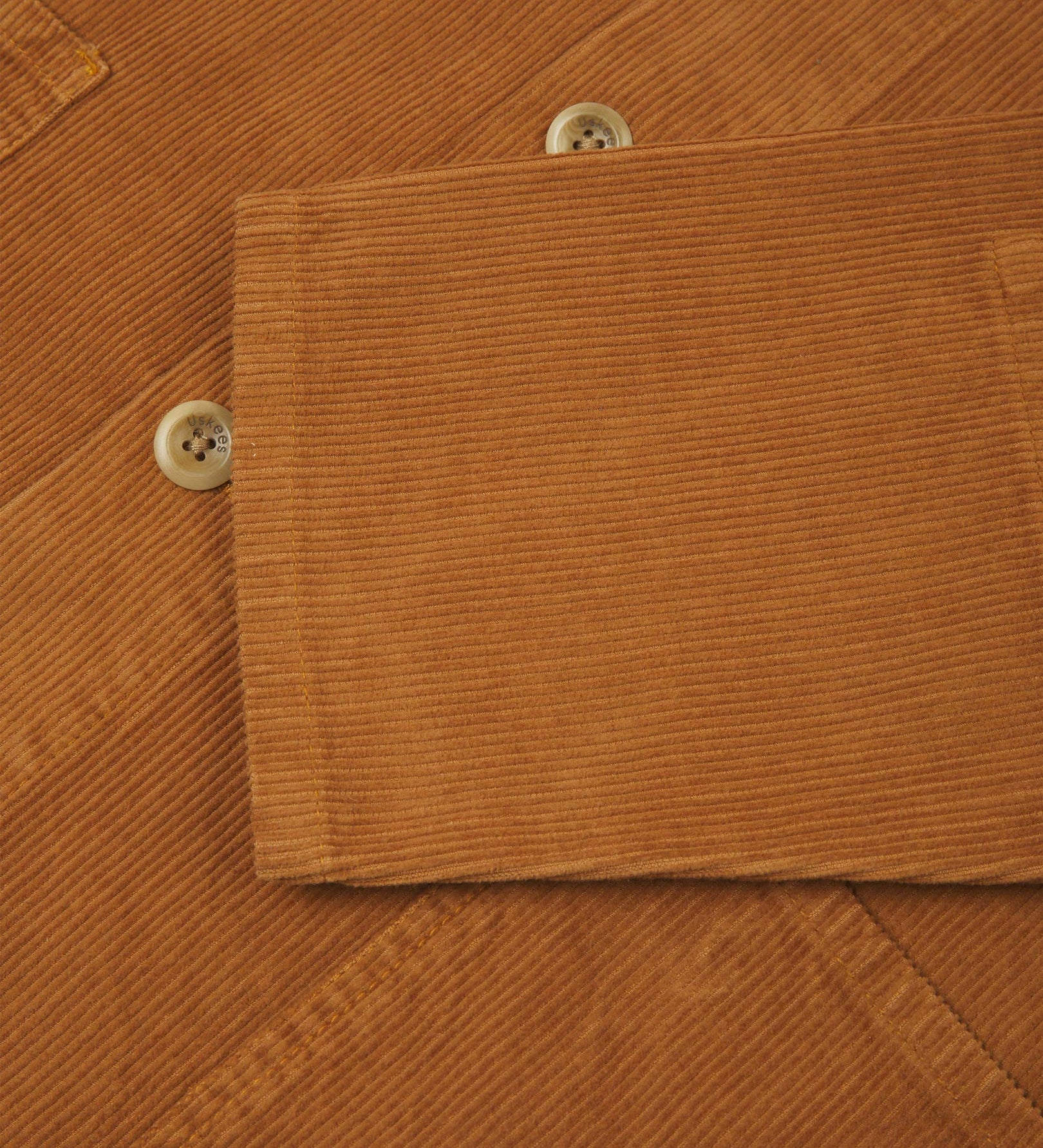 Closer view of mid section of tan, buttoned corduroy overshirt from Uskees. Focus on cuff, pockets, corozo buttons and corduroy texture.