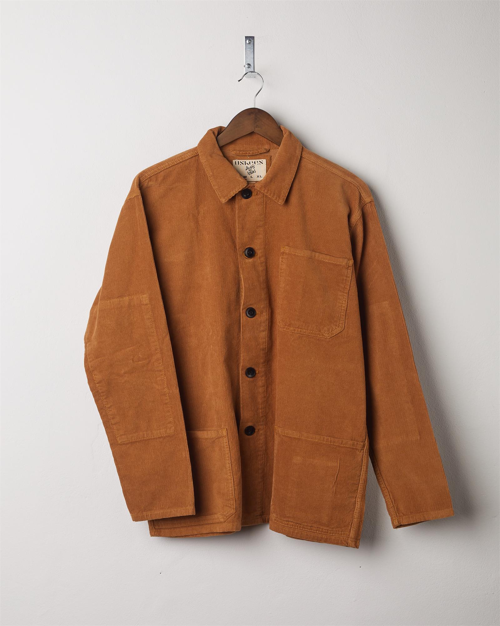 Tan coloured, buttoned corduroy overshirt from Uskees presented on hanger. Clear view of breast and hip pocket and corozo buttons.
