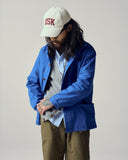 model wearing an ultra blue uskees shacket, cream baseball cap with 'USK' text, and casual outfit on a plain background.
