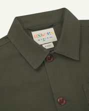 Front close-up flat shot of an uskees dull green men's overshirt showing brown corozo buttons and brand label at neck.