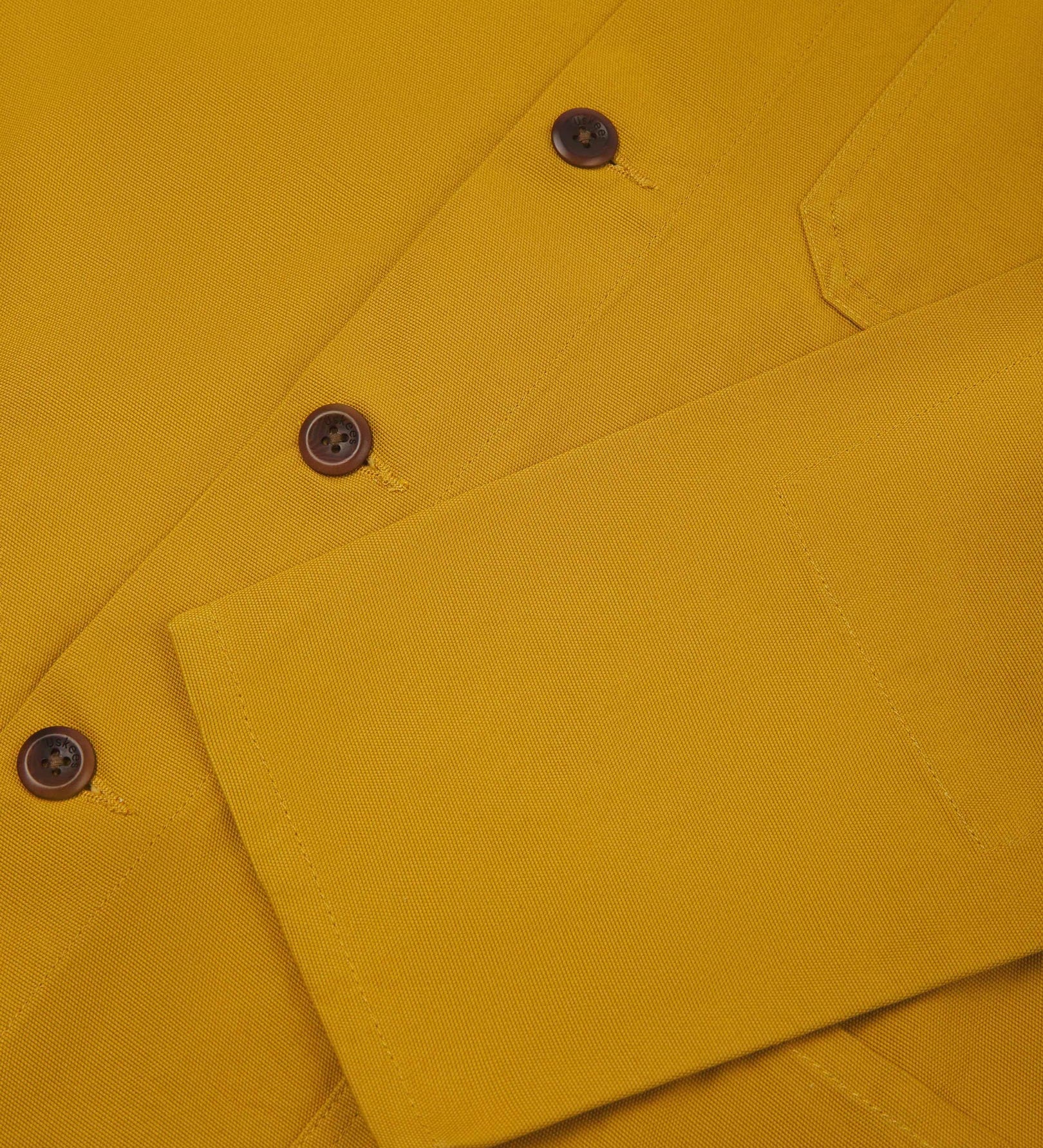 Closer view of mid section of yellow, buttoned organic cotton overshirt from Uskees. Focus on cuff, pockets and corozo buttons.