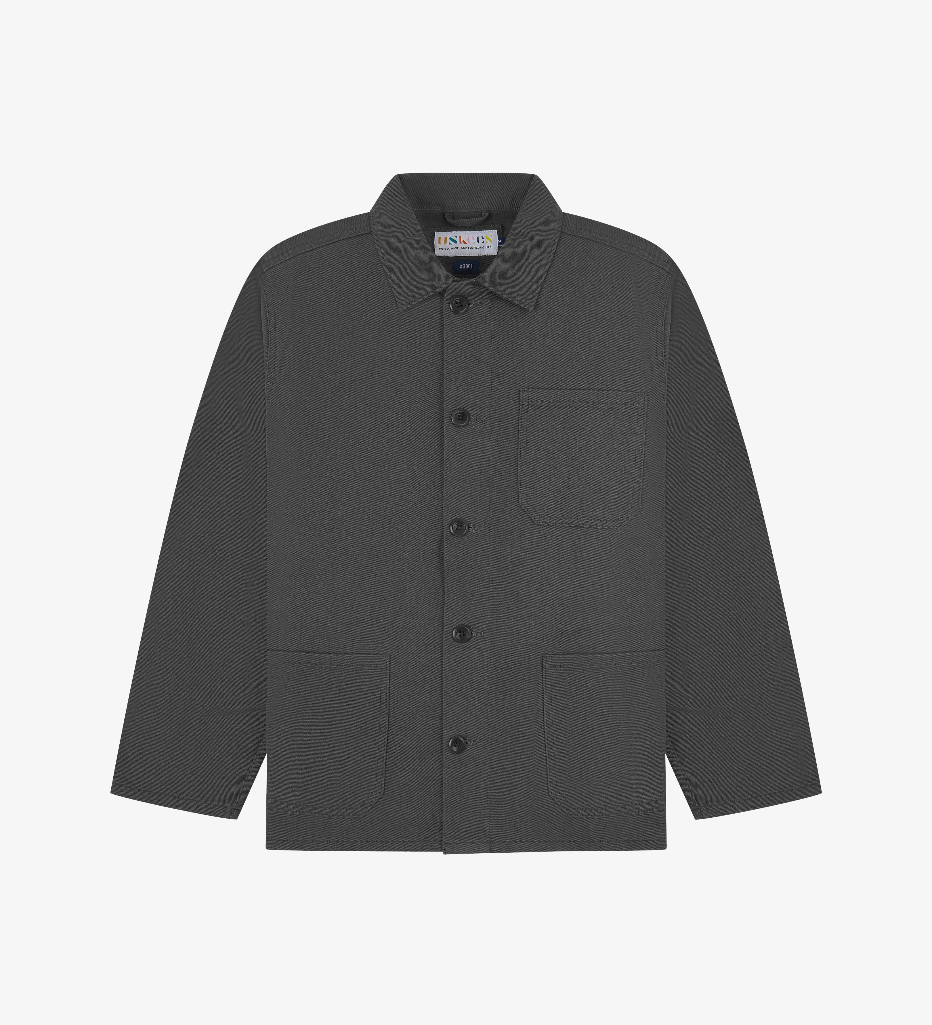 Front flat shot of charcoal-grey, buttoned drill overshirt. Clear view of corozo buttons, 3 pockets and Uskees branding label.