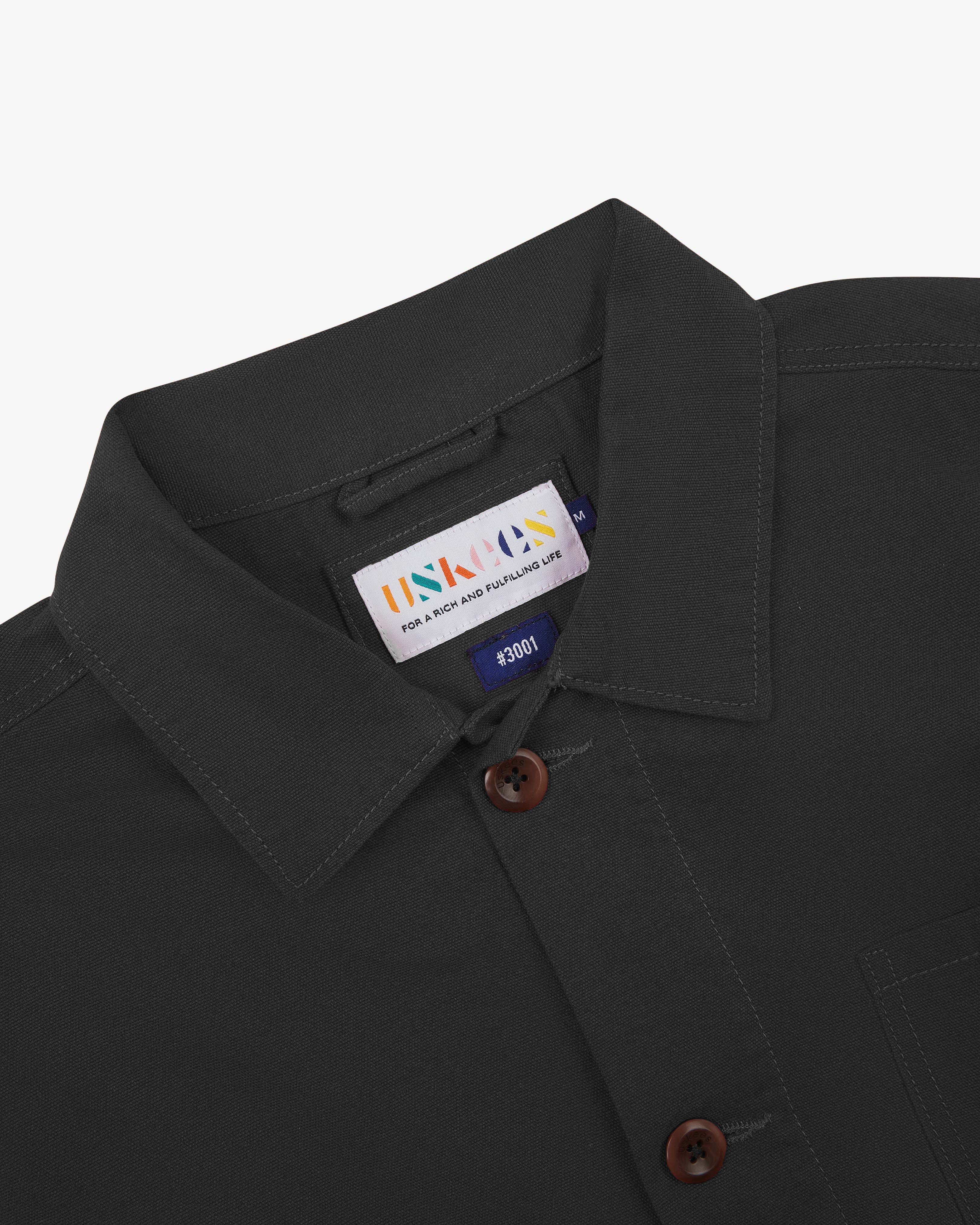 Close-up view of 3001 charcoal-grey, buttoned organic cotton overshirt from Uskees showing corozo buttons, brand label, collar and hanging hoop.