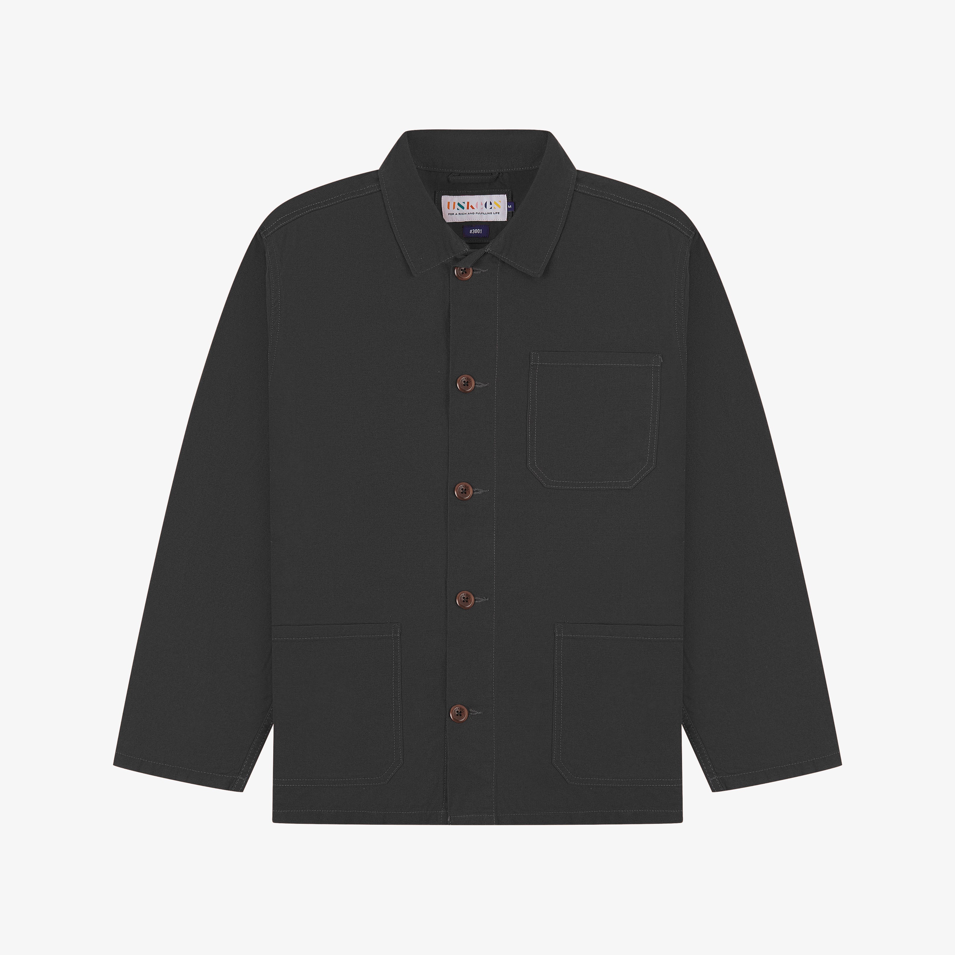 Front flat shot of charcoal-grey, buttoned organic cotton overshirt. Clear view of chest and hip pockets, corozo buttons and Uskees branding label.