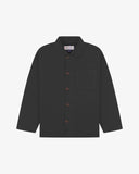Front flat shot of charcoal-grey, buttoned organic cotton overshirt. Clear view of chest and hip pockets, corozo buttons and Uskees branding label.