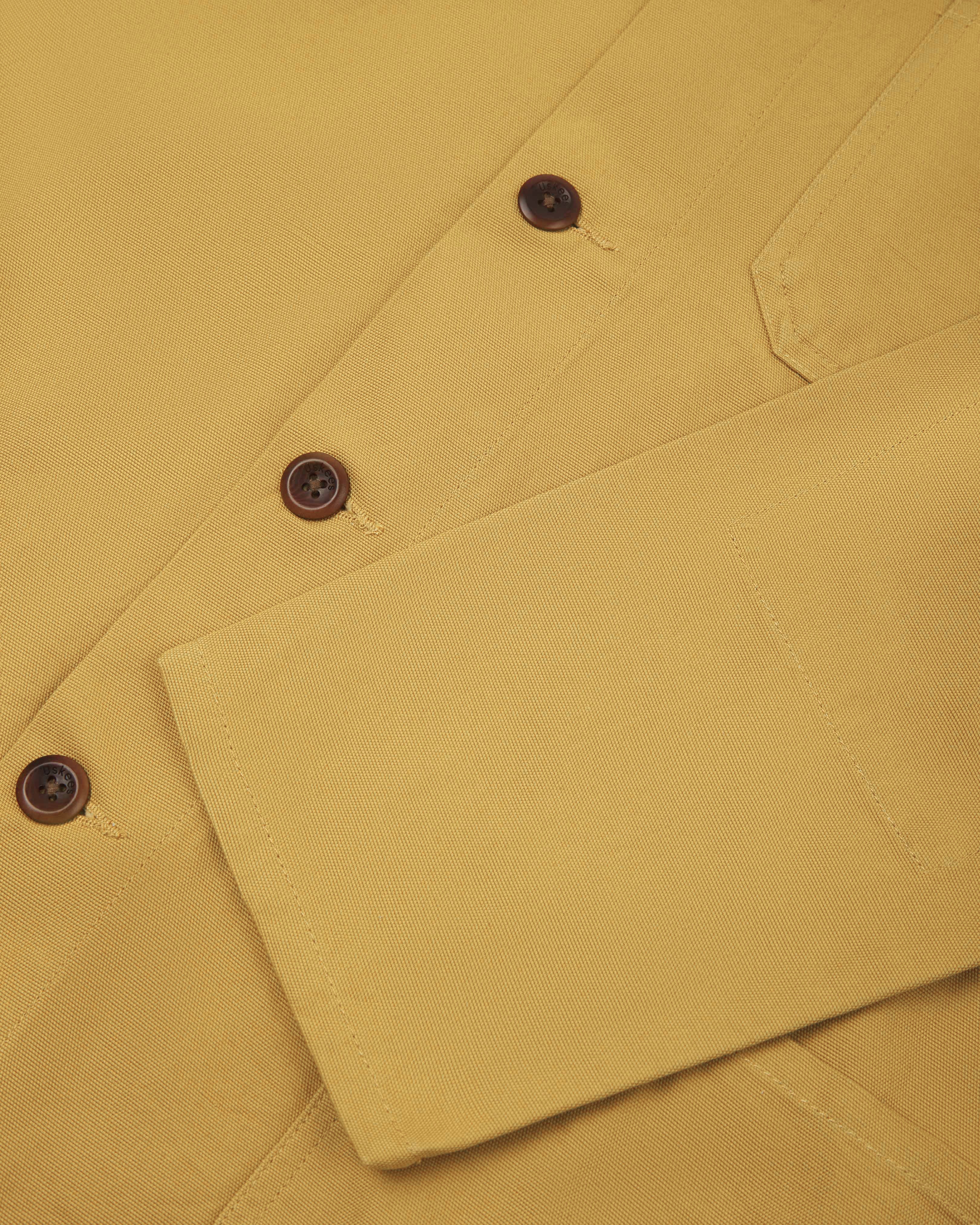 Close up shot of the front of an uskees yellow men's overshirt showing  plant based corozo buttons and sleeve detail.