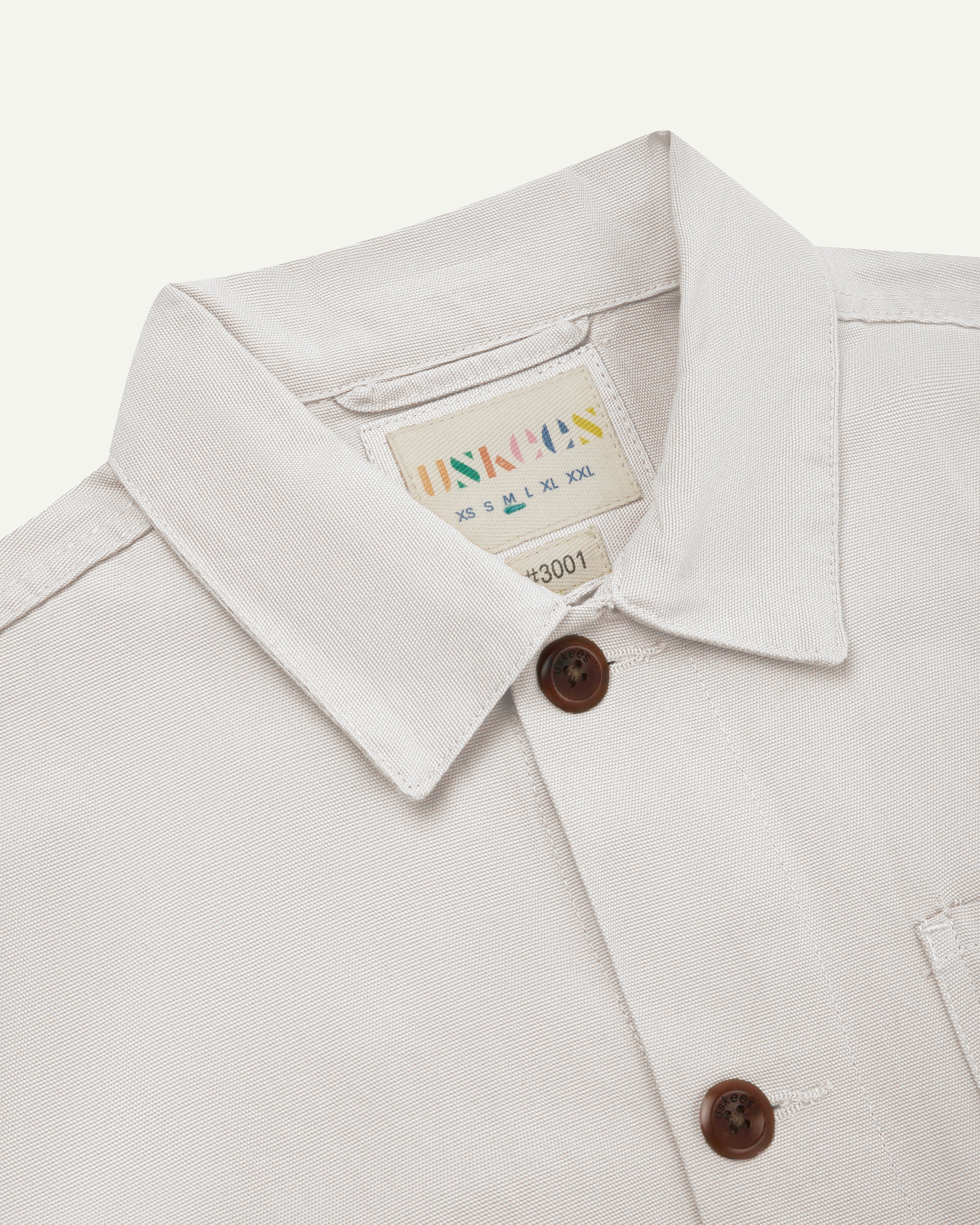 Front close shot of an uskees cream men's overshirt showing contrast brown corozo buttons and brand/size label at neck.