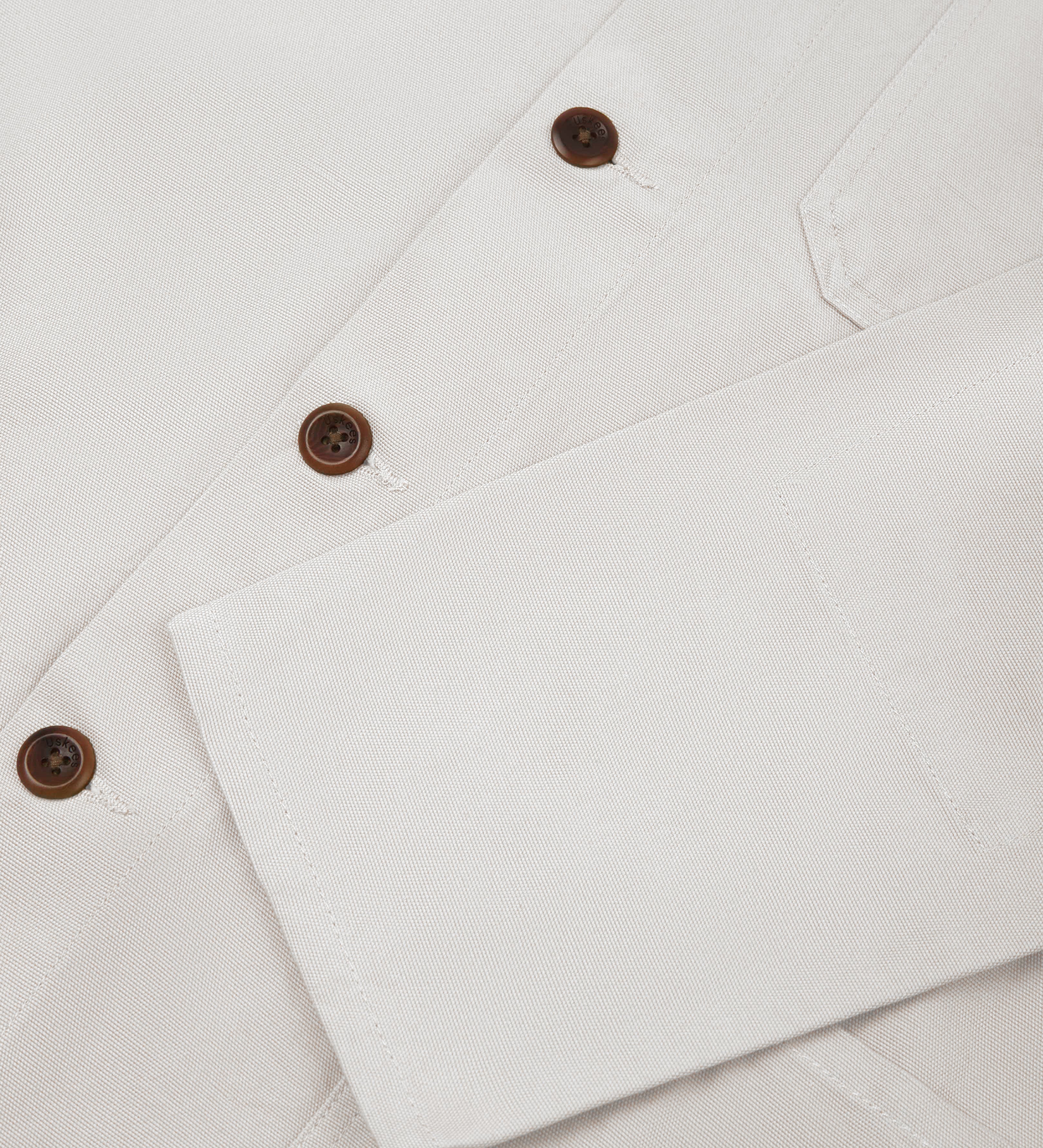 Close up shot of the front of an uskees cream men's overshirt showing contrast plant based corozo buttons and sleeve detail.