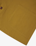 Close-up of an Uskees mustard yellow overshirt pocket presented on a white background