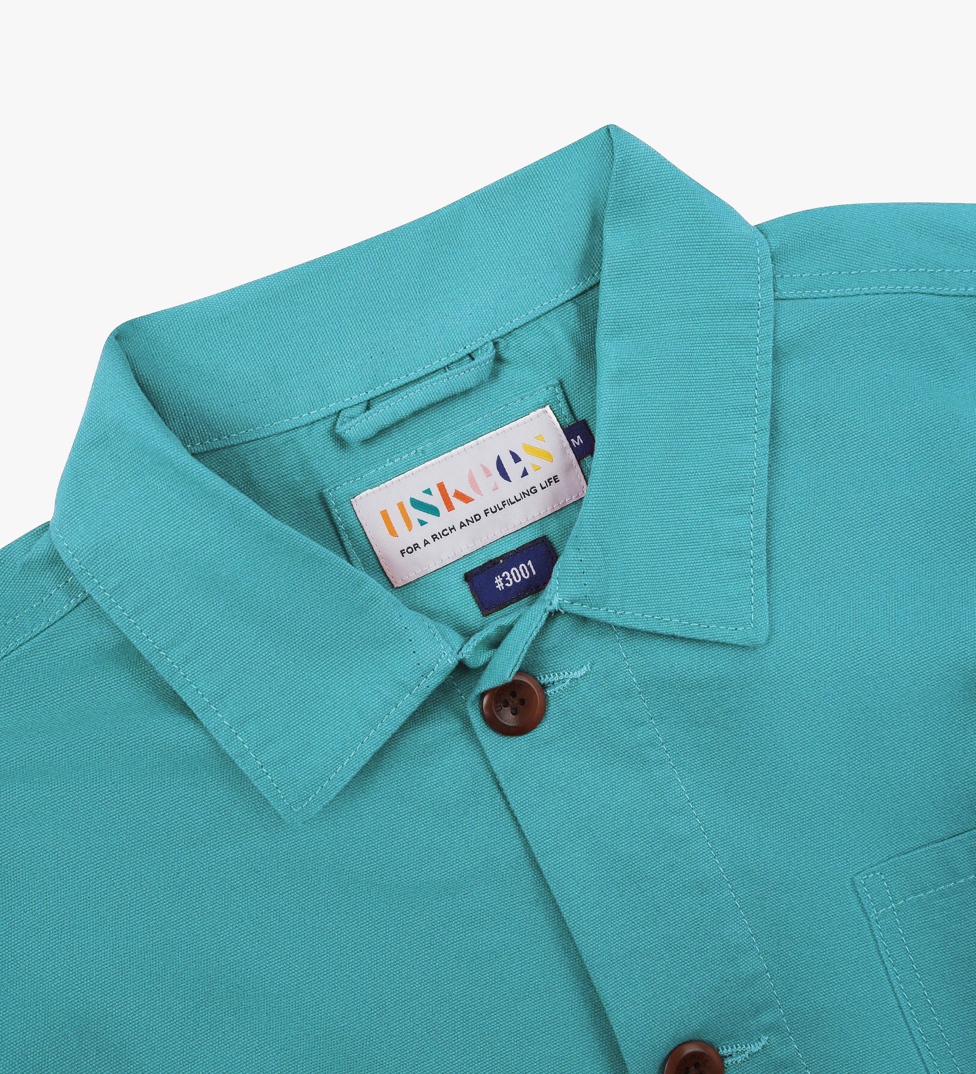 Close-up shot of turquoise blue overshirt collar showing the Uskees brand label, on a white background.