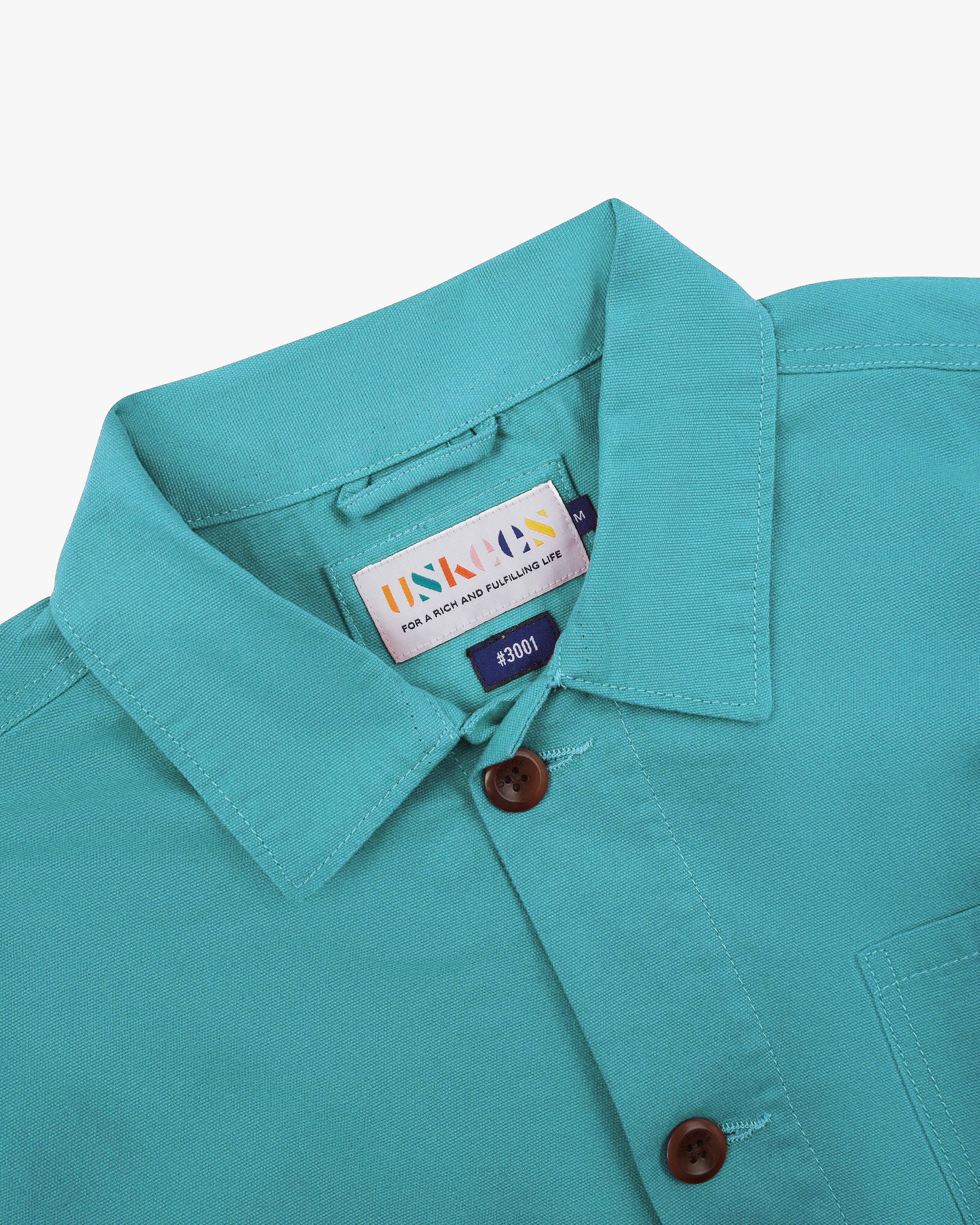 Close-up shot of turquoise blue overshirt collar showing the Uskees brand label, on a white background.