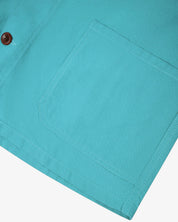 Close-up of a aqua blue shirt-jacket pocket and brown Corozo button on a white background