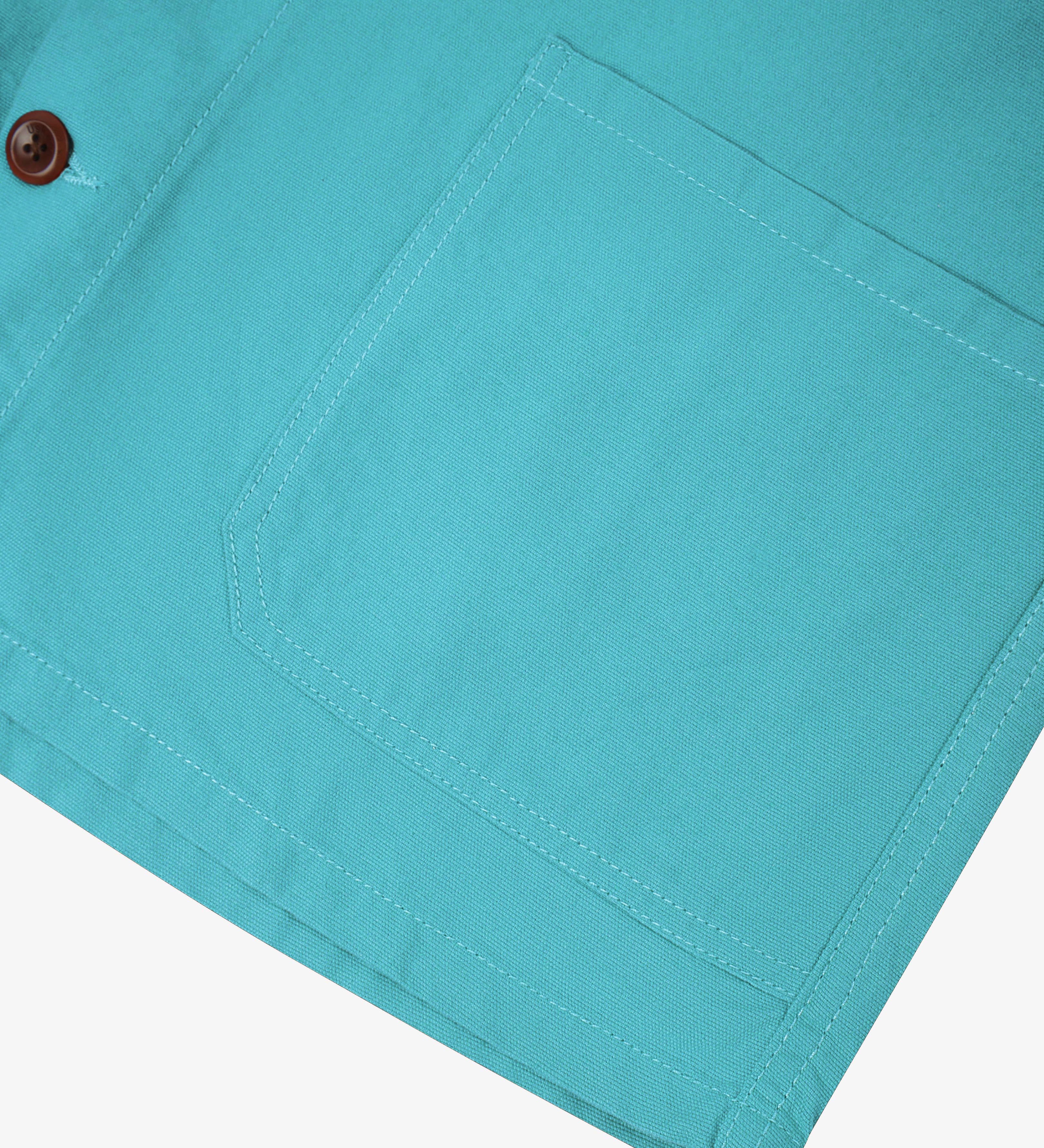 Close-up of a aqua blue shirt-jacket pocket and brown Corozo button on a white background