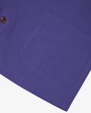 Close up of an Uskees purple shirt jacket showing the brown Corozo button and patch pocket, presented on a light gray background