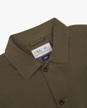 Close-up of a green/brown uskees overshirt collar showing the brand label on a white background