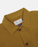 Close-up of a mustard yellow Uskees shirt jacket for men showing the brand label, presented on a white background