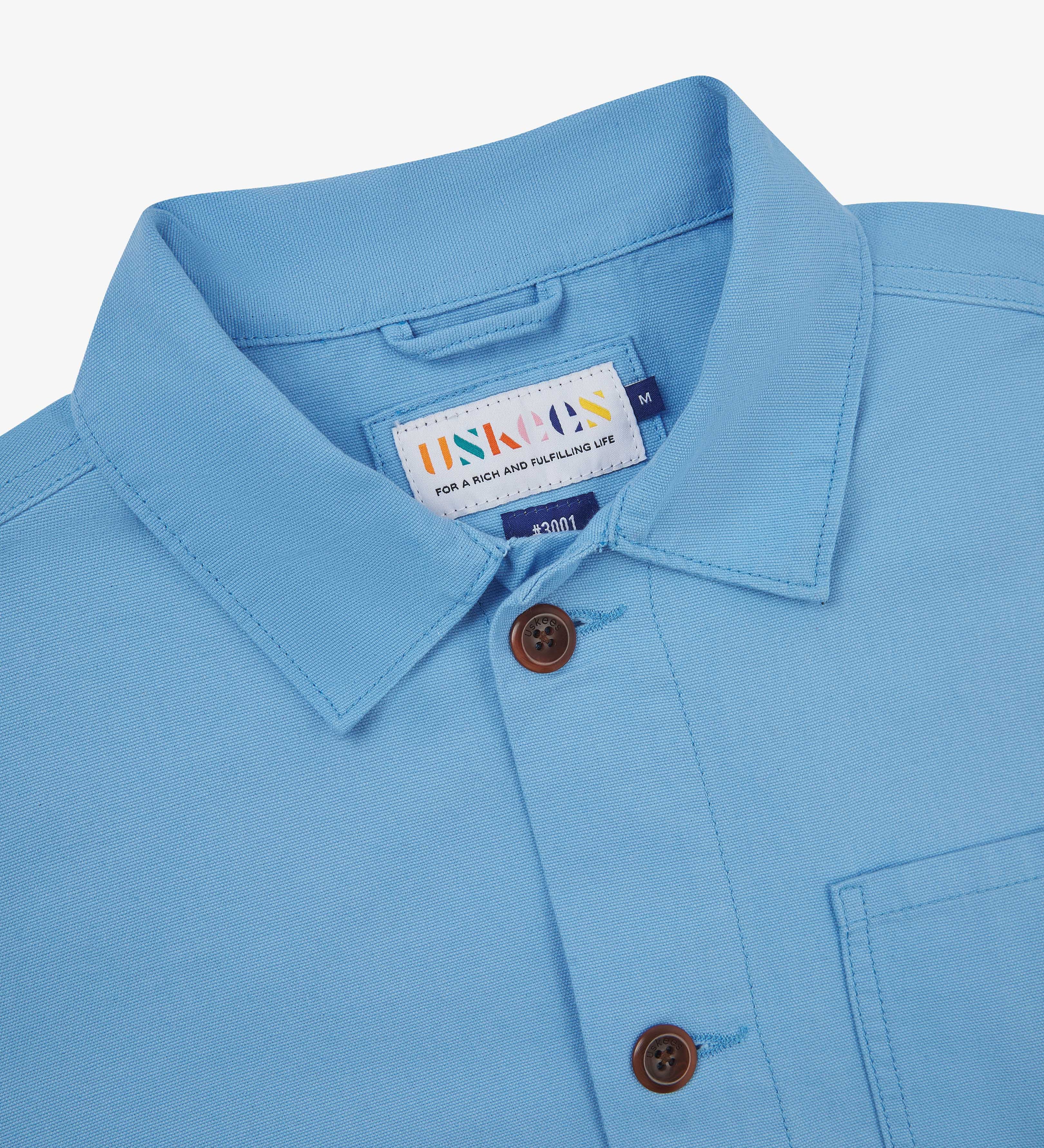 Close-up of an Uskees powder blue overshirt with a brand label on a white background