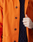 Close-up of a male model wearing a bright orange Uskees button-front overshirt for men over a navy blue cable-knit sweater.