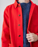 A close-up of a person wearing a bright red button-front overshirt over a textured blue knit sweater, with one hand pulling the overshirt open slightly.