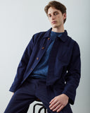 A male model wearing an Uskees navy blue overshirt and matching trousers over a textured blue knit sweater, posed against a light gray studio background.