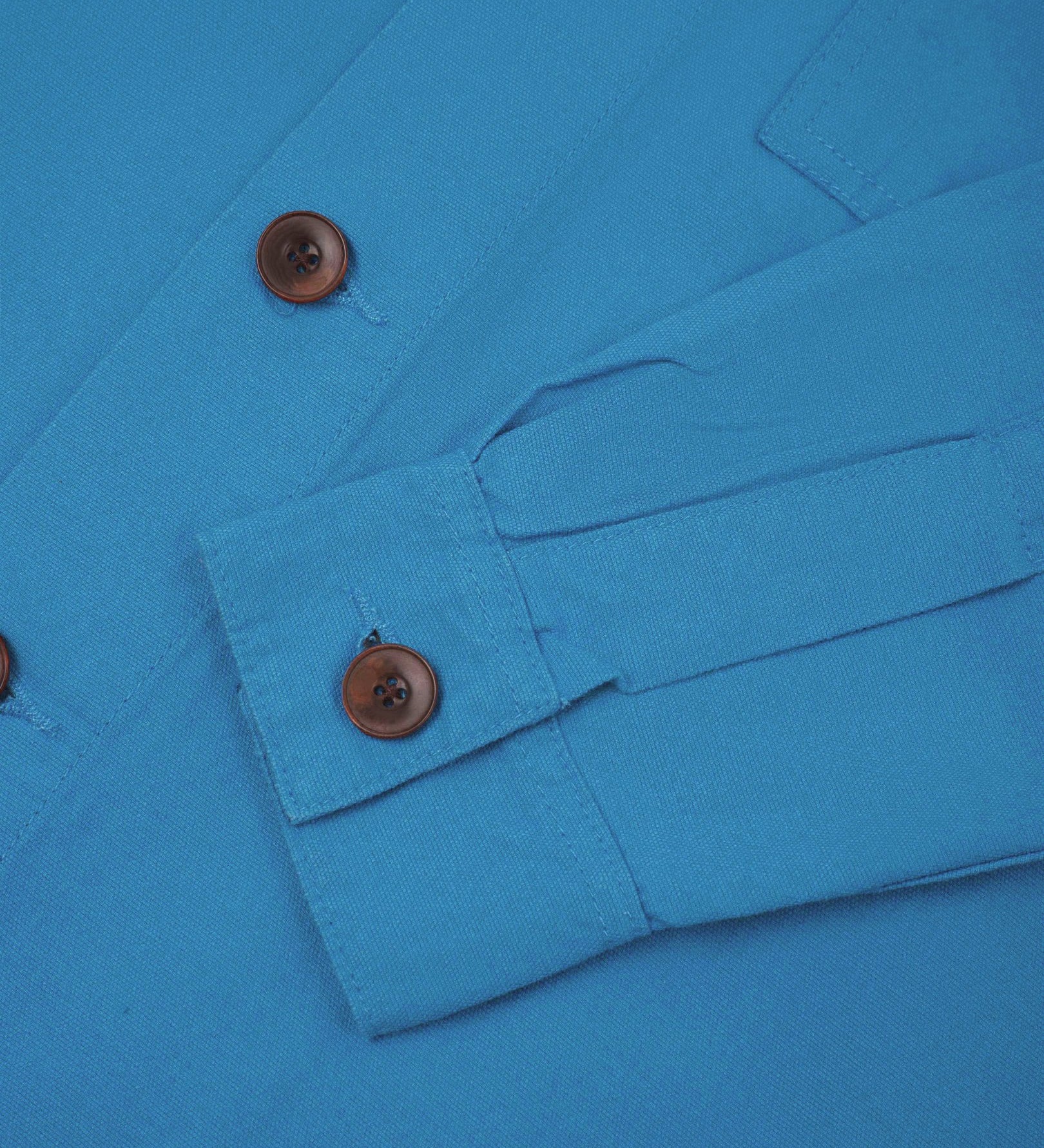 View of the mid-section and sleeve of the 3003 Uskees button-down work shirt in bright blue with focus on cuff, placket and corozo buttons.