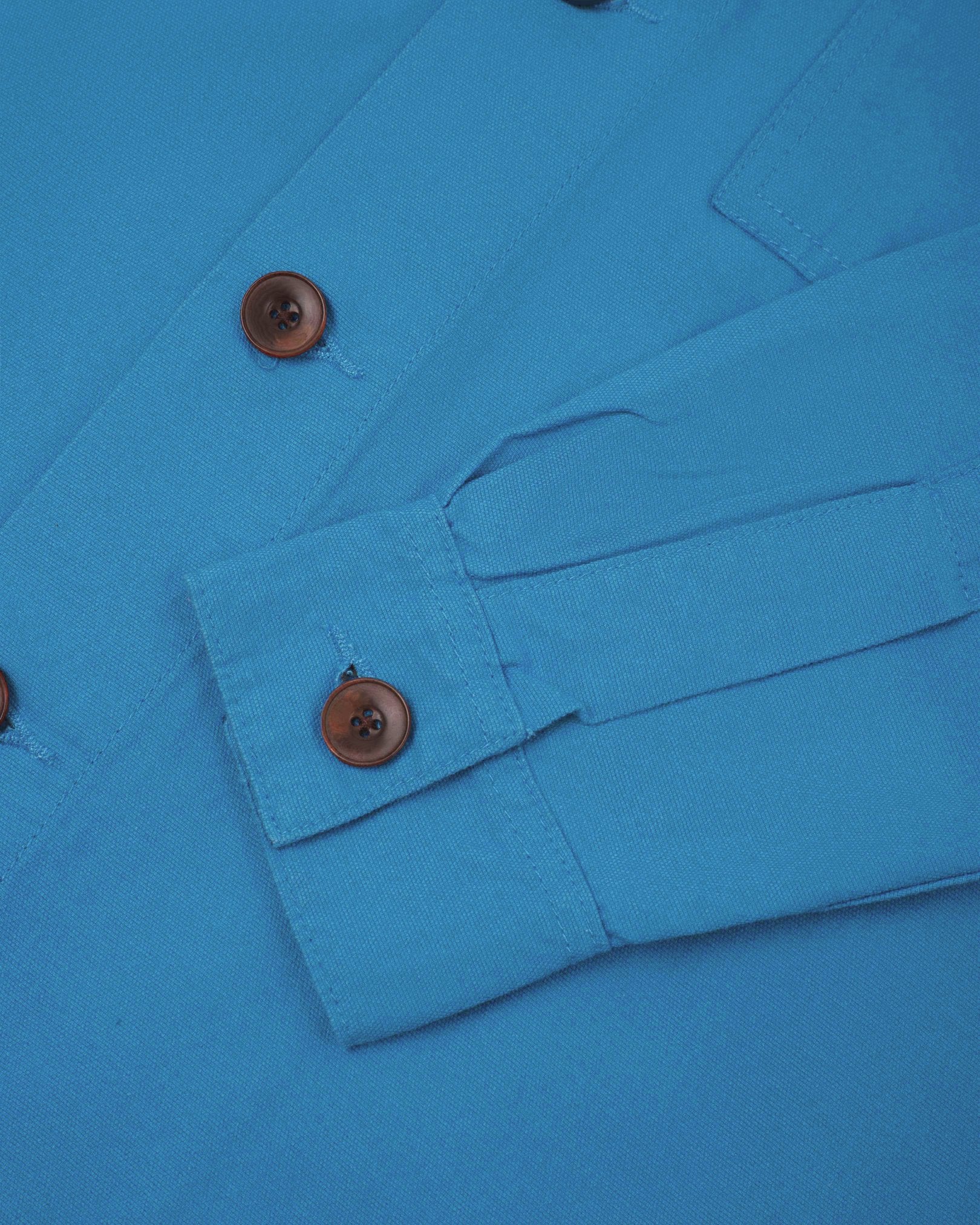 View of the mid-section and sleeve of the 3003 Uskees button-down work shirt in bright blue with focus on cuff, placket and corozo buttons.