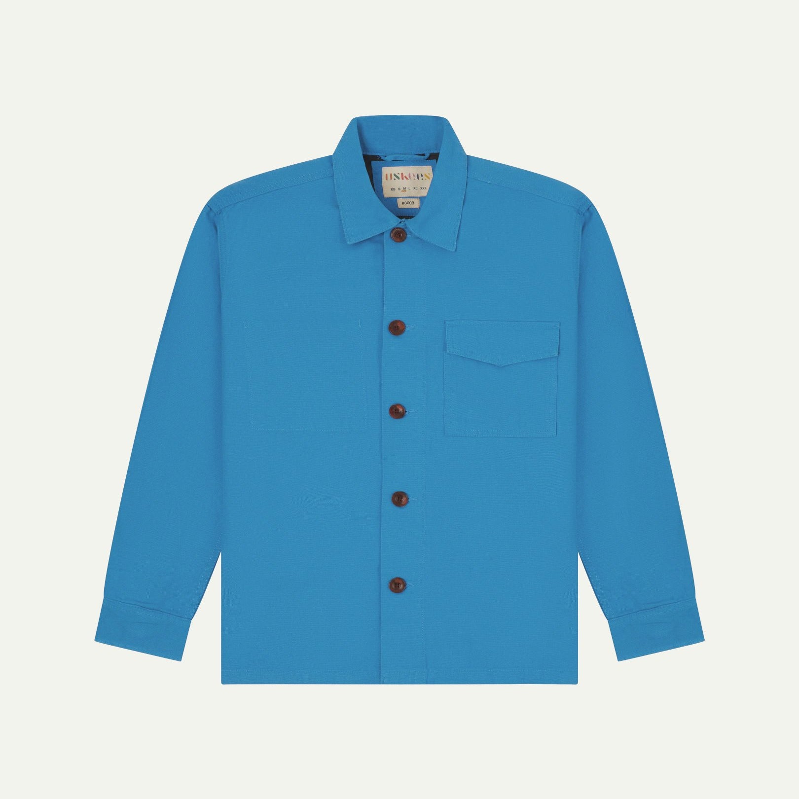 Bright blue buttoned organic cotton workshirt from Uskees with clear view of chest pocket and Uskees branding label.