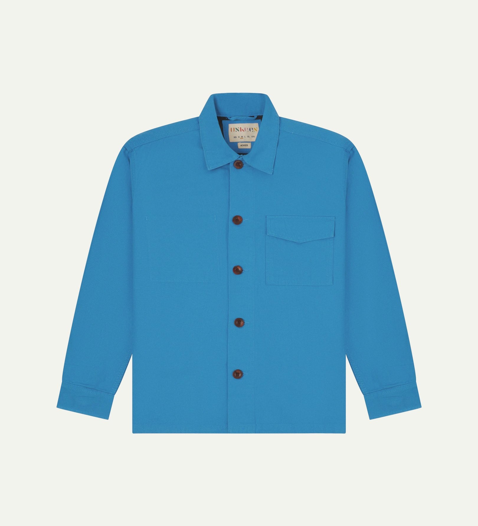 Bright blue buttoned organic cotton workshirt from Uskees with clear view of chest pocket and Uskees branding label.