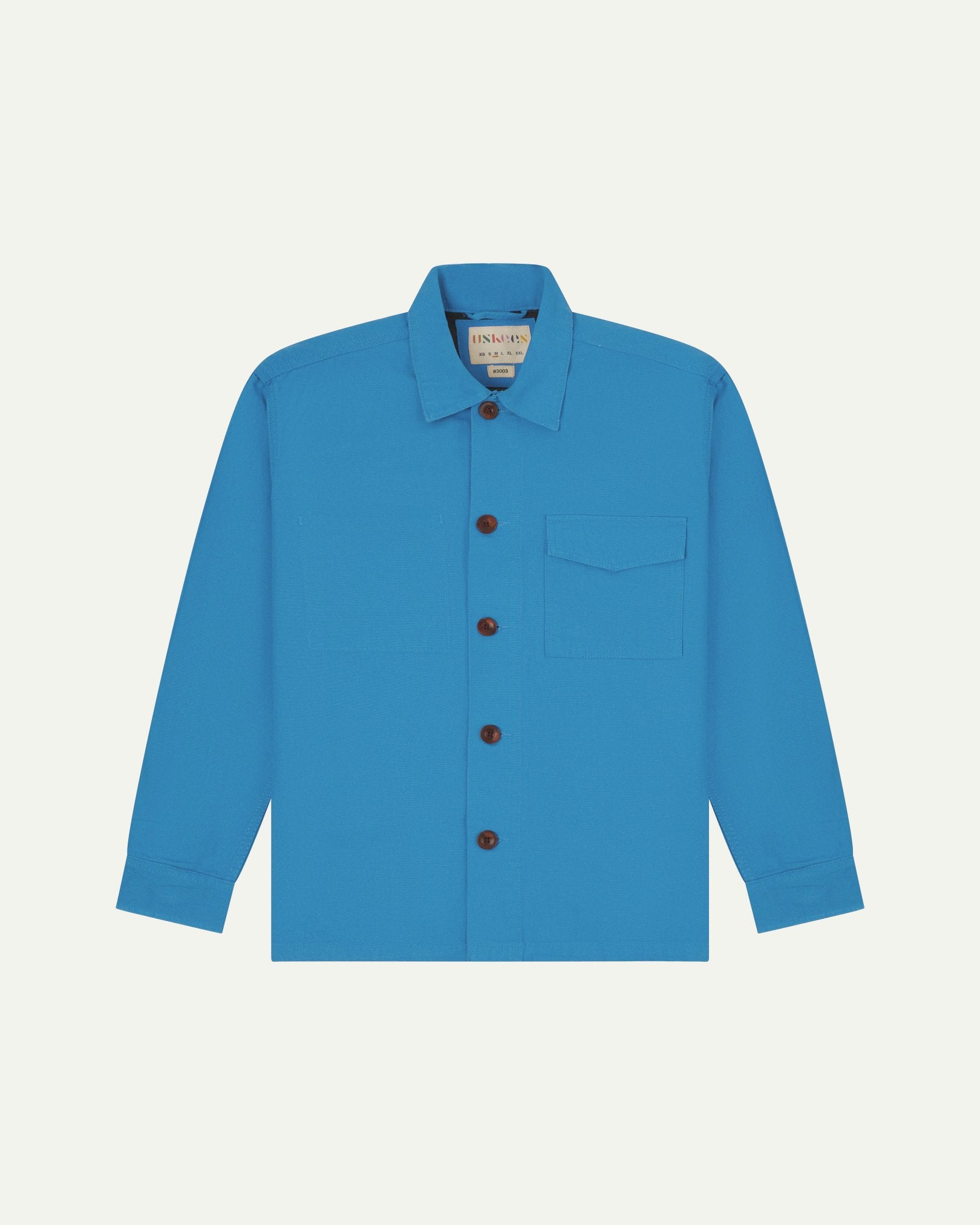 Bright blue buttoned organic cotton workshirt from Uskees with clear view of chest pocket and Uskees branding label.