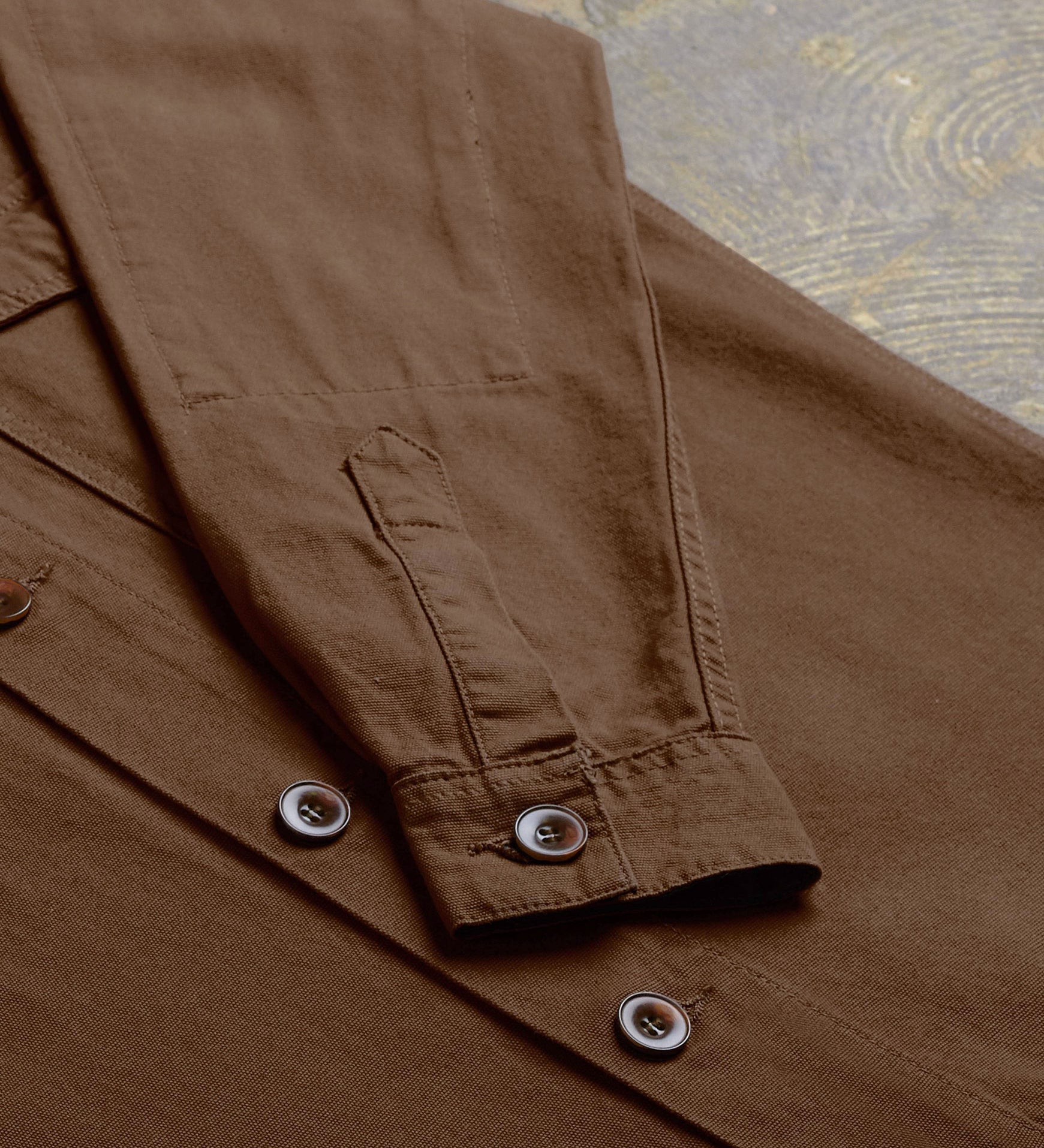Angled flat view of the mid-section and sleeve of the #3003 Uskees button-down work shirt in brown, with focus on cuff, placket, reinforced elbow and corozo buttons.