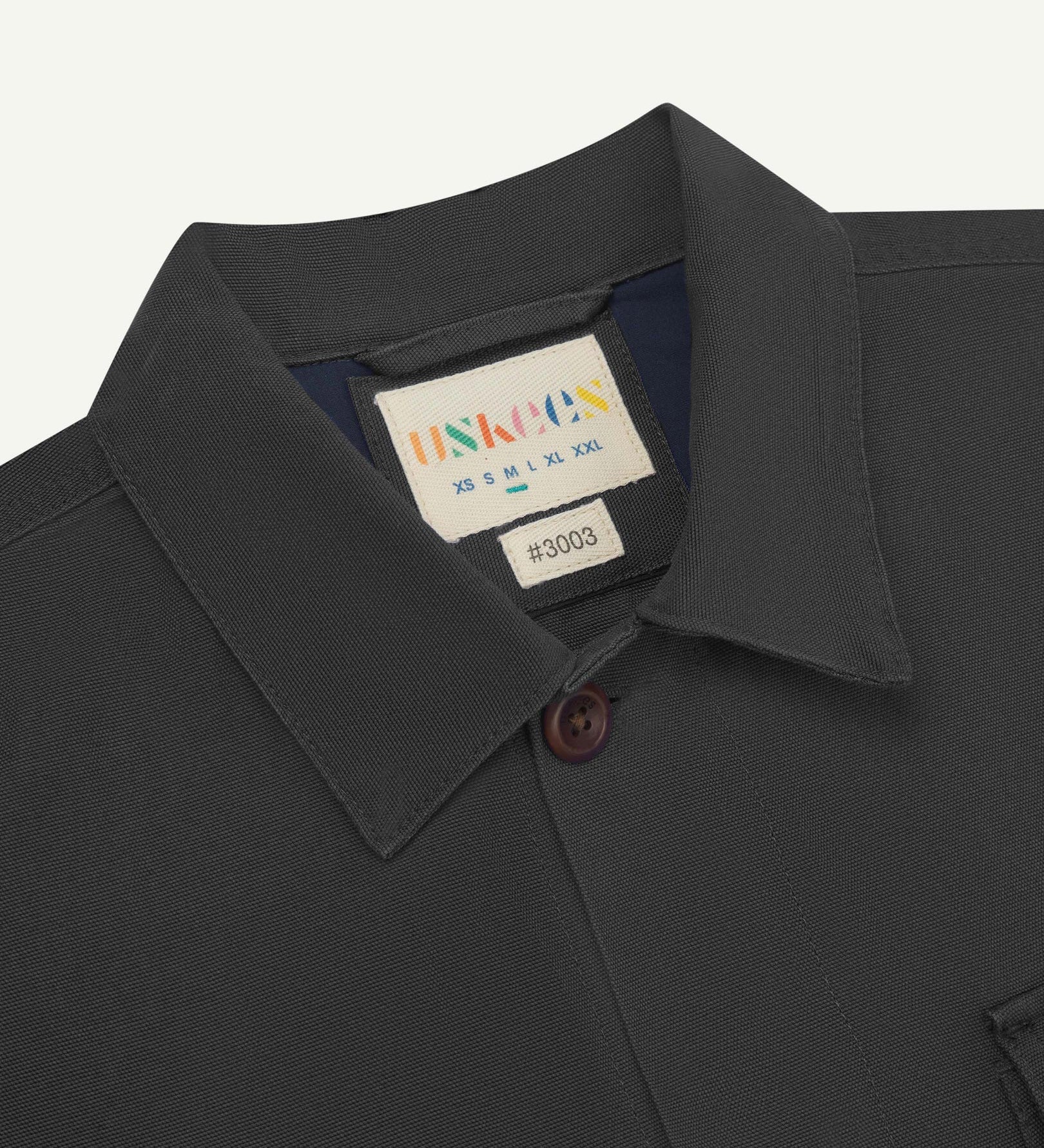 Close-up top-half view of #3003, charcoal organic cotton workshirt. With focus on collar, Uskees brand label and corozo buttons.