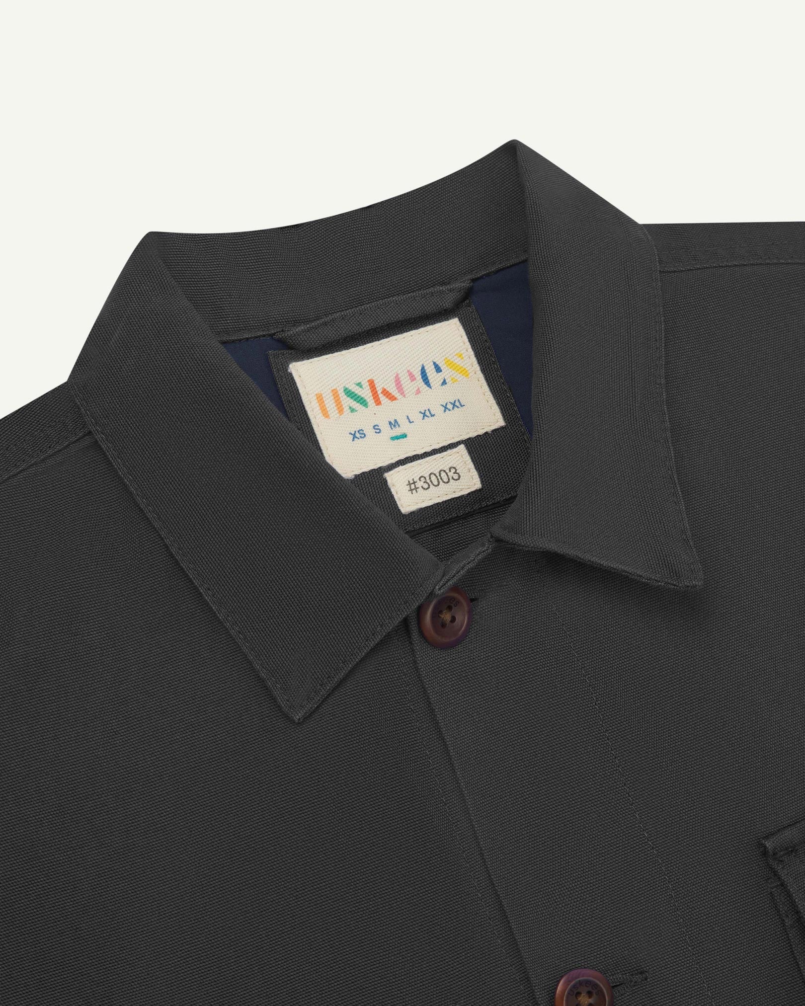 Close-up top-half view of #3003, charcoal organic cotton workshirt. With focus on collar, Uskees brand label and corozo buttons.